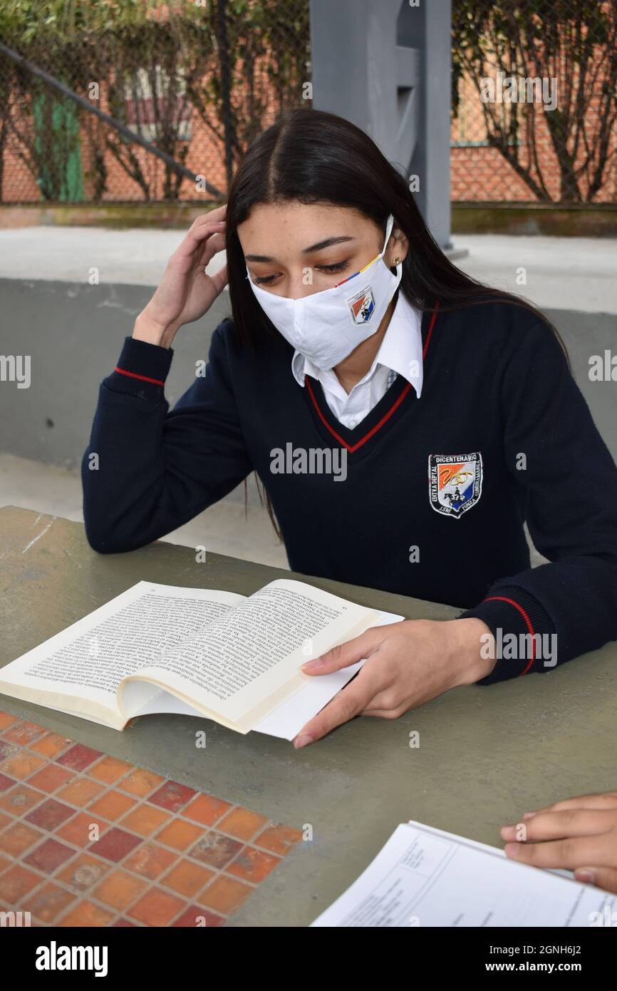 MOSQUERA, COLOMBIE - 31 août 2021 : une jeune étudiante de sexe féminin lisant un livre en étant assise dans la salle de classe avec un masque de sécurité Banque D'Images