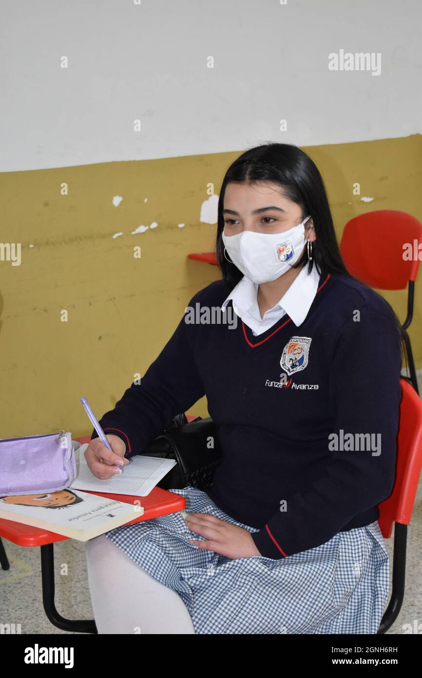 MOSQUERA, COLOMBIE - 31 août 2021 : une jeune étudiante de sexe féminin prend des notes tout en étant assise dans la salle de classe avec un masque de sécurité Banque D'Images