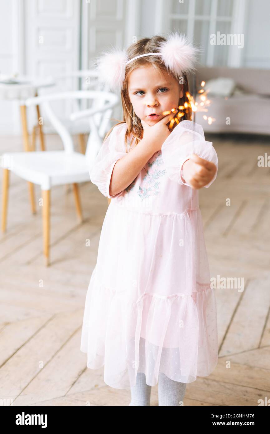 Drôle petite fille mignonne avec de longs cheveux dans robe rose clair tenant la bougie flambante dans les mains dans le salon lumineux à la maison. Noël, birt Banque D'Images