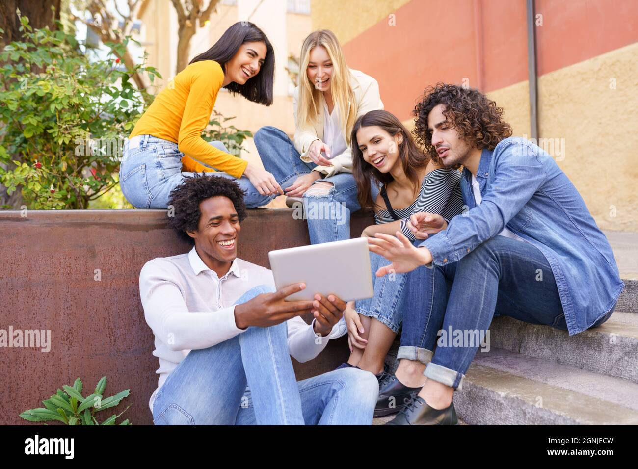 Groupe multiethnique de jeunes qui regardent une tablette numérique à l'extérieur en milieu urbain. Banque D'Images