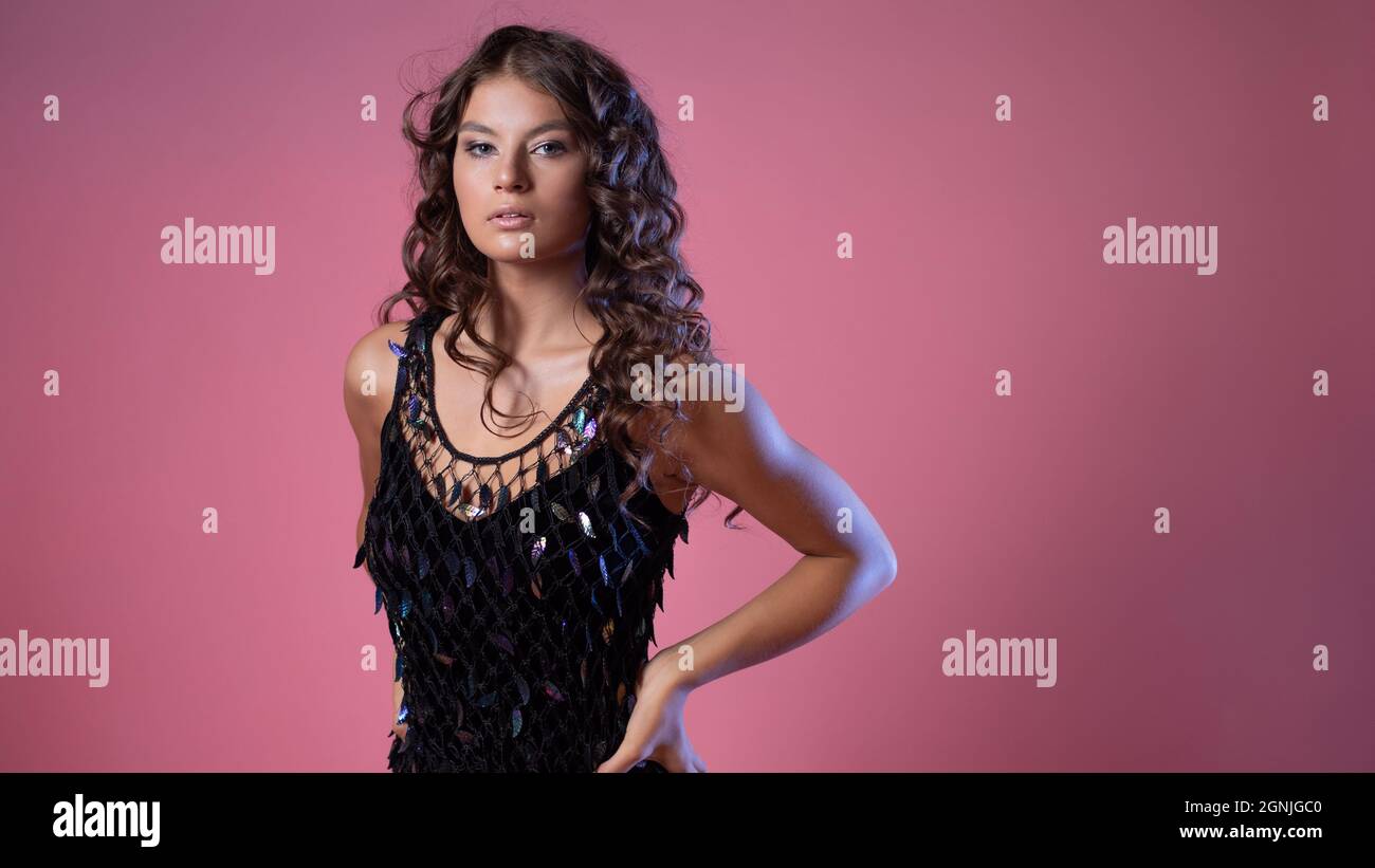 Élégante dame dans une robe longue de soirée noire avec des paillettes, portrait d'une belle jeune brune sur fond rose Banque D'Images