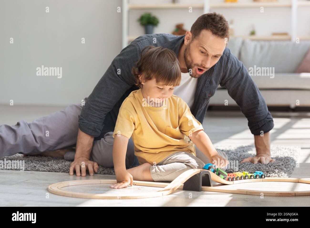 Concept familial convivial. Mignon petit garçon jouant train avec son papa, surpris homme regardant le jouet avec excitation Banque D'Images