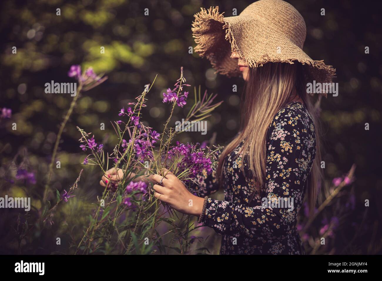 Jeune femme avec chapeau d'été, sentant des fleurs violettes Banque D'Images
