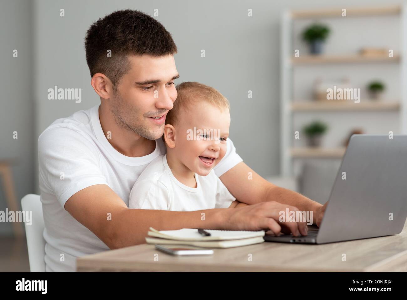 Congé de paternité. Jeune homme travaillant sur un ordinateur portable à la maison avec bébé son Banque D'Images