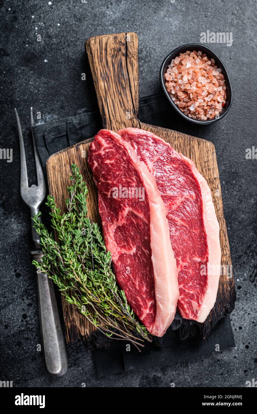 Steak de rumsteck cru non cuit ou biftecks de viande de bœuf au chapeau de sirloin sur une planche de bois. Arrière-plan noir. Vue de dessus Banque D'Images