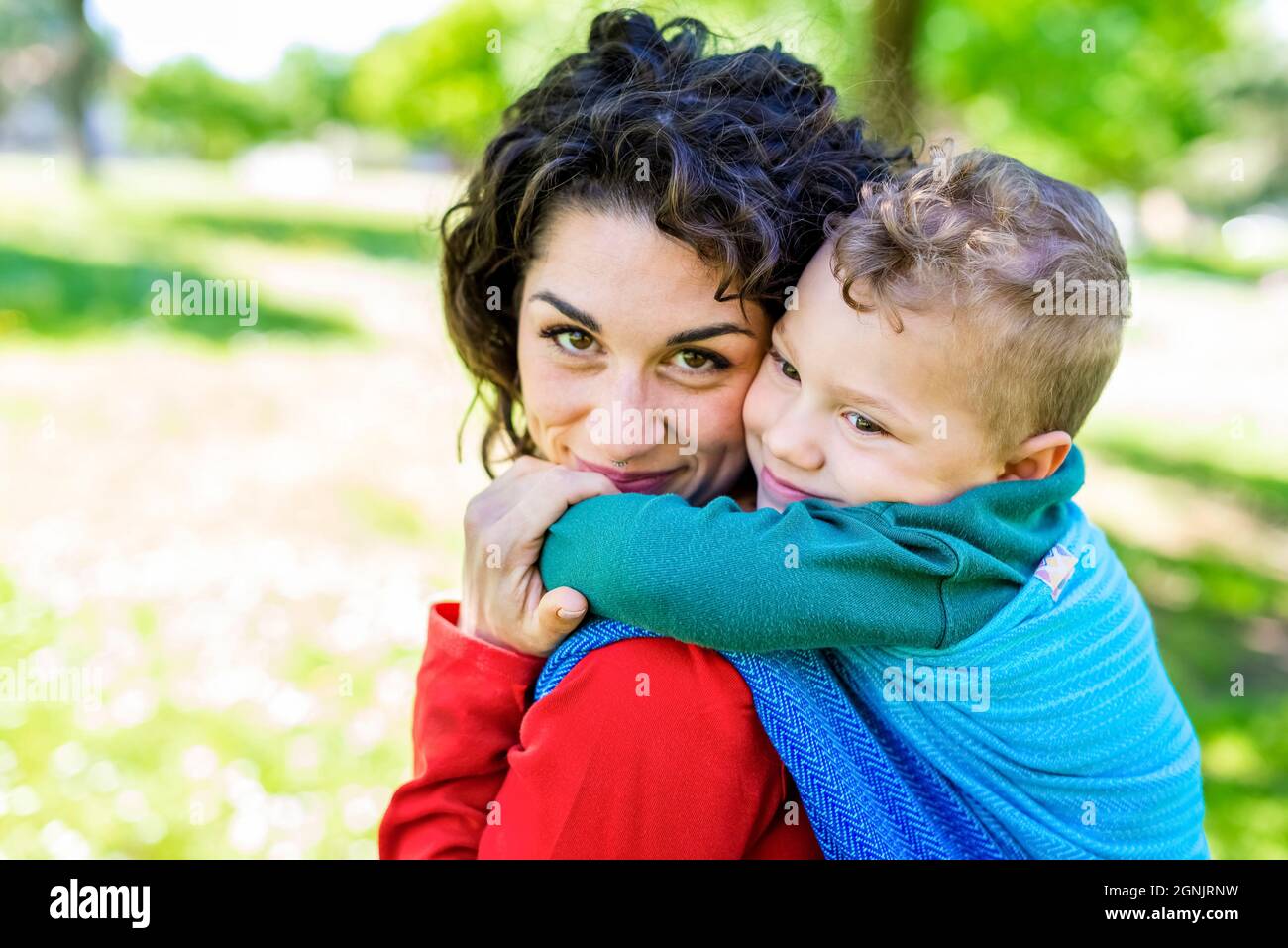 portrait rapproché d'une jeune maman heureuse porte un enfant sur son dos attaché avec un morceau de tissu traditionnel coloré dans un jardin de parc public. mère Banque D'Images