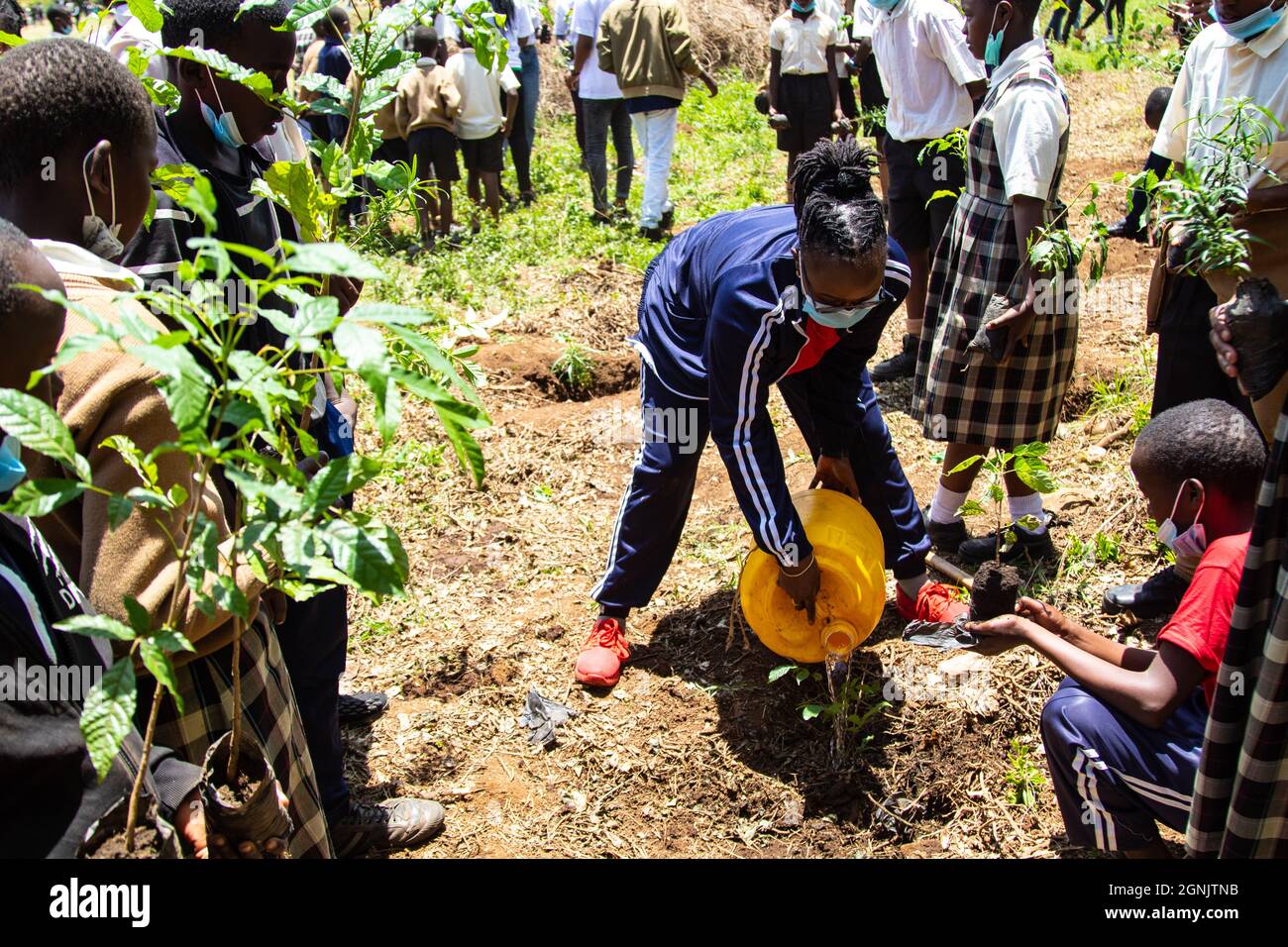 Une enseignante en costume de survêtement est entourée par ses élèves alors  qu'elle arrose une plantule pendant un vendredi pour une manifestation  future.les activistes du climat à Nakuru le 24 septembre 2021