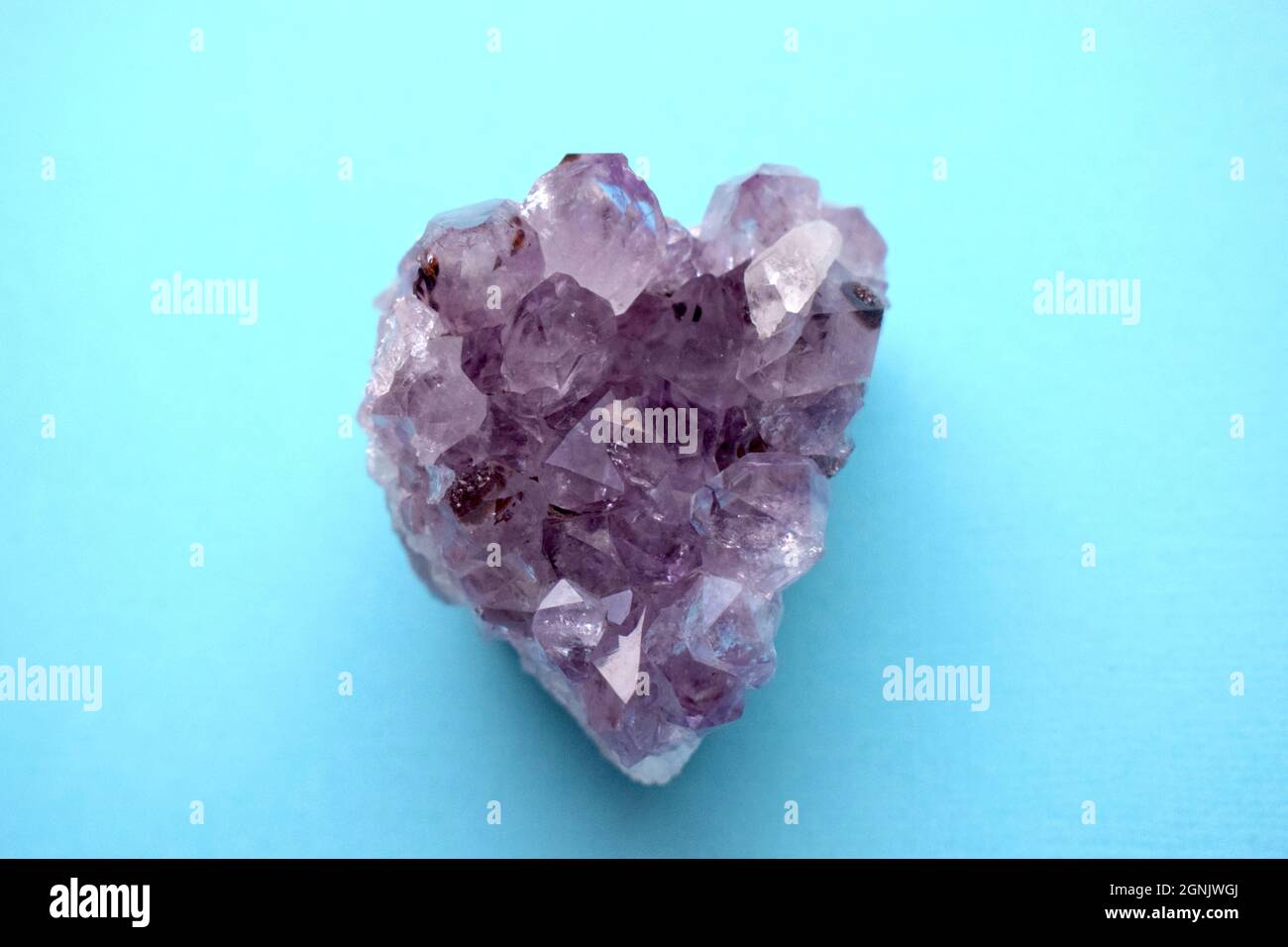 Belle drase d'améthyste minéral violet naturel sous forme de coeur sur fond bleu. De grands cristaux d'un bijou. Banque D'Images