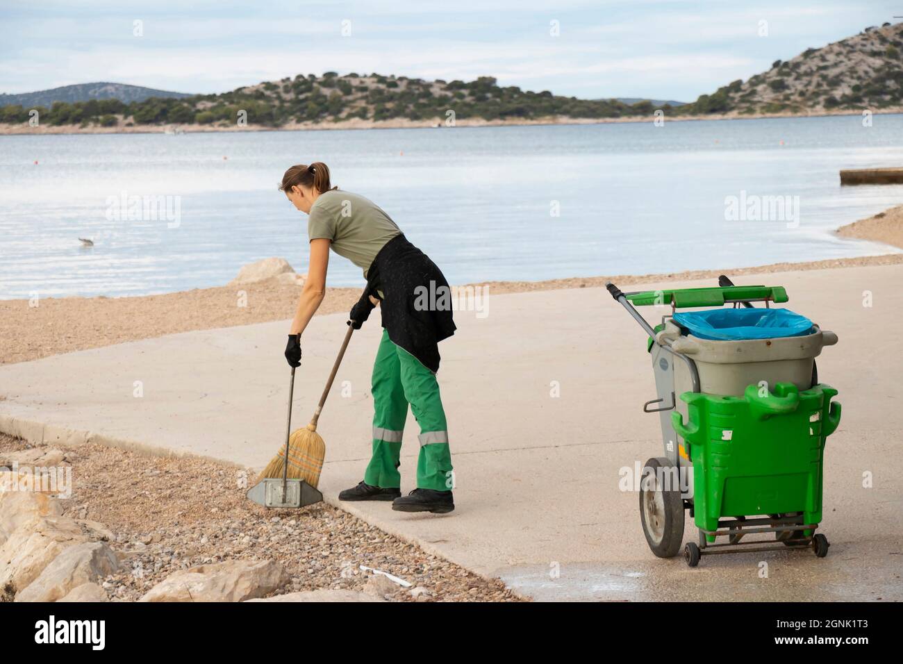 Vodice, Croatie - 28 août 2021: Jeune femme de ménage, travaillant pour le service de ville de Lec, sur son service de routine matinale de nettoyage de la plage Banque D'Images
