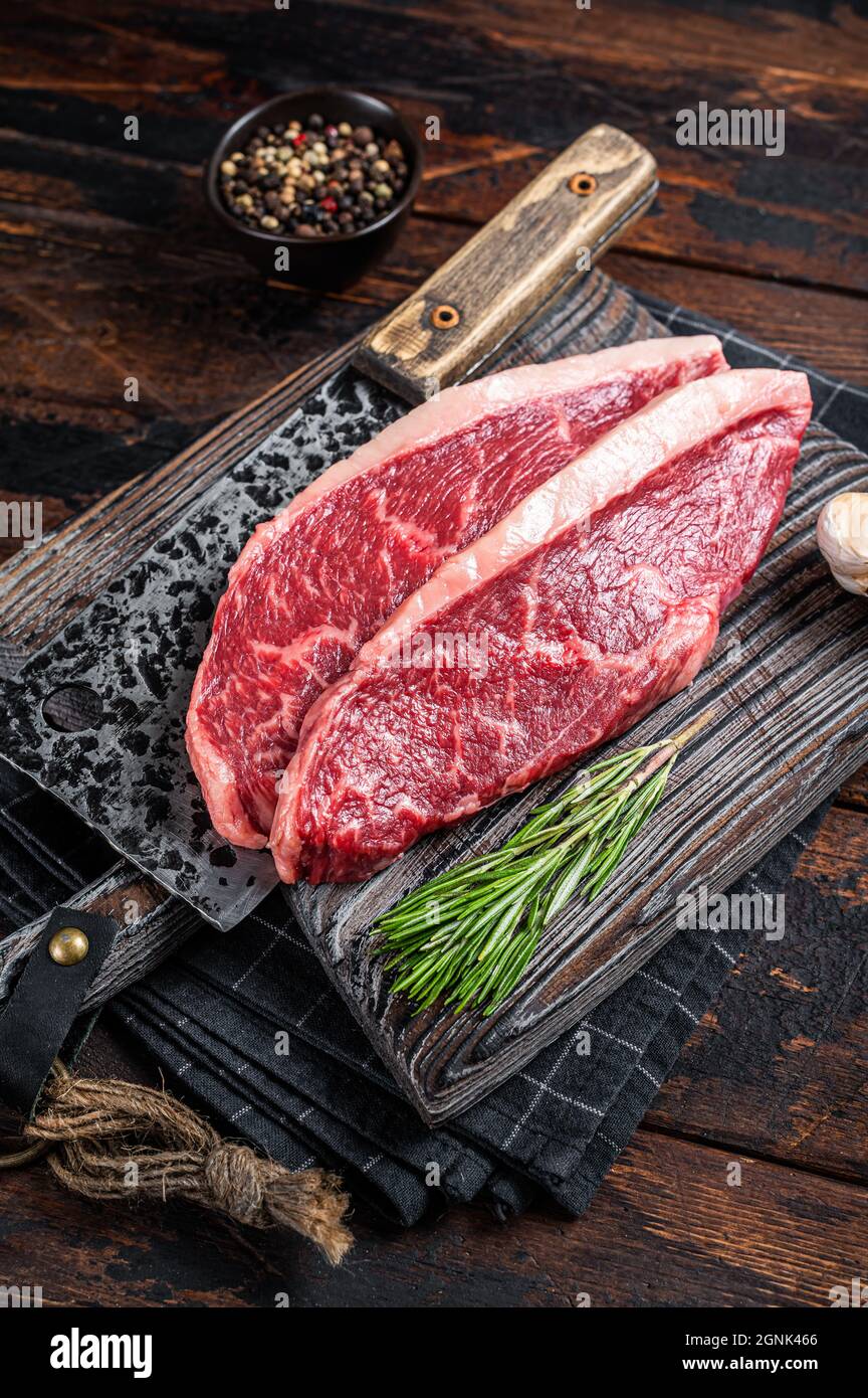 Steaks de viande de bœuf sur le dessus de la cicloine crue sur le butboard avec le cale à viande. Arrière-plan sombre. Vue de dessus Banque D'Images