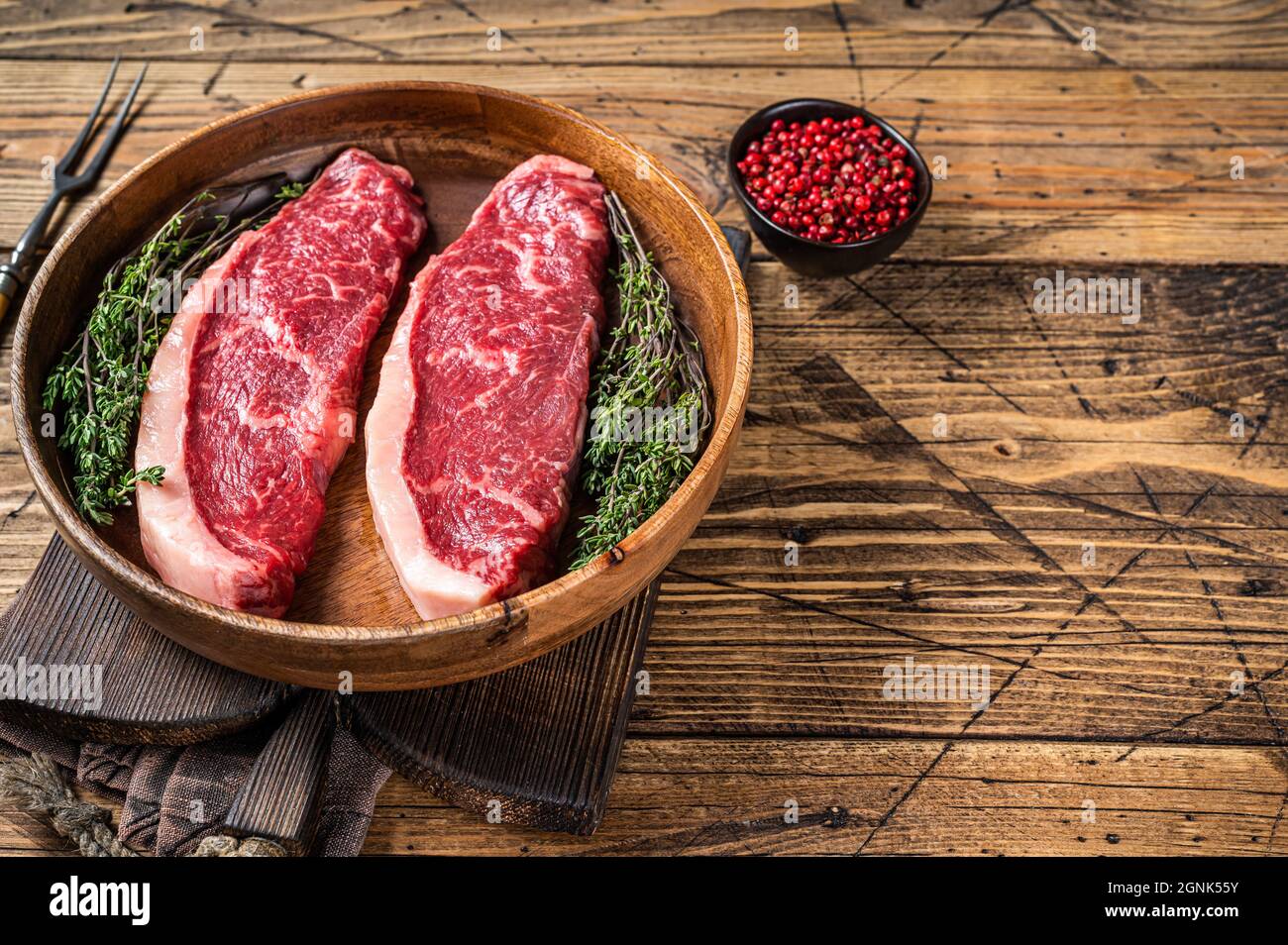 Steaks de viande de boeuf non cuits en haut cru au sommet de sirloin dans une assiette en bois avec des herbes. fond de woden. Vue de dessus. Copier l'espace Banque D'Images