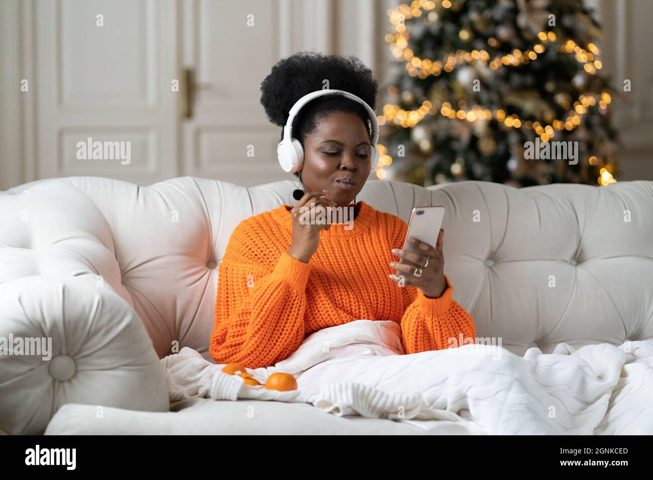 Une femme africaine passe le matin de noël à la maison dans le salon avec arbre de Noël lire les sms dans le smartphone Banque D'Images