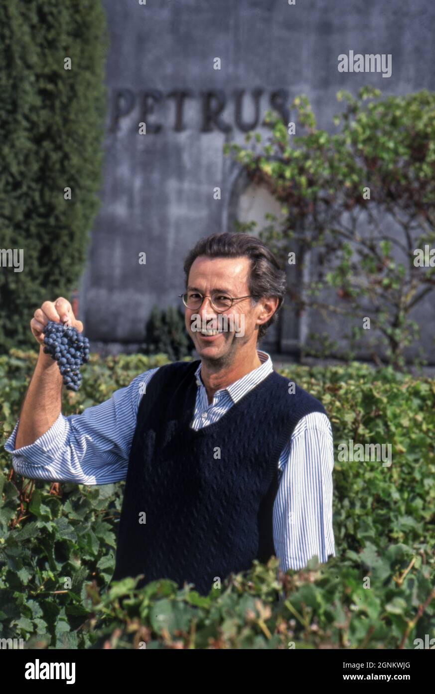 Château Petrus vendange c2002 Christian Moueix (propriétaire légendaire)  souriant avec fierté un bouquet de raisins mûrs parfaits au moment de la  récolte dans le vignoble du Château Pétrus, Pomerol, Gironde, France Photo