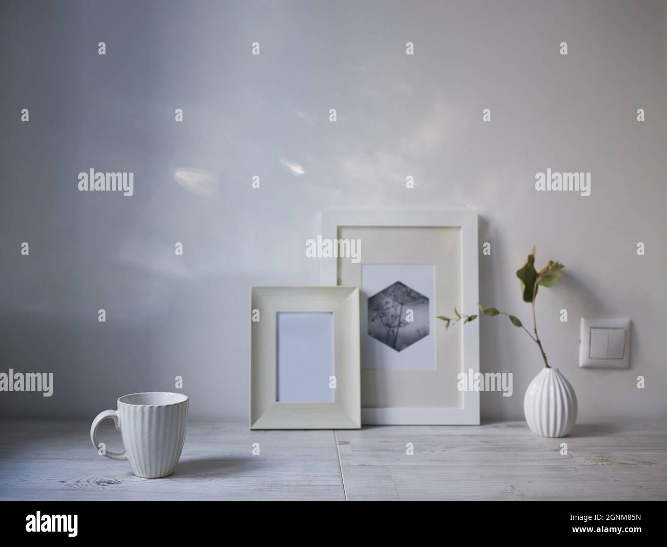 Style scandinave. Design intérieur. Une tasse blanche, un petit vase avec une branche d'eucalyptus séché, deux cadres photo sont sur la table. Copier l'espace pour tex Banque D'Images