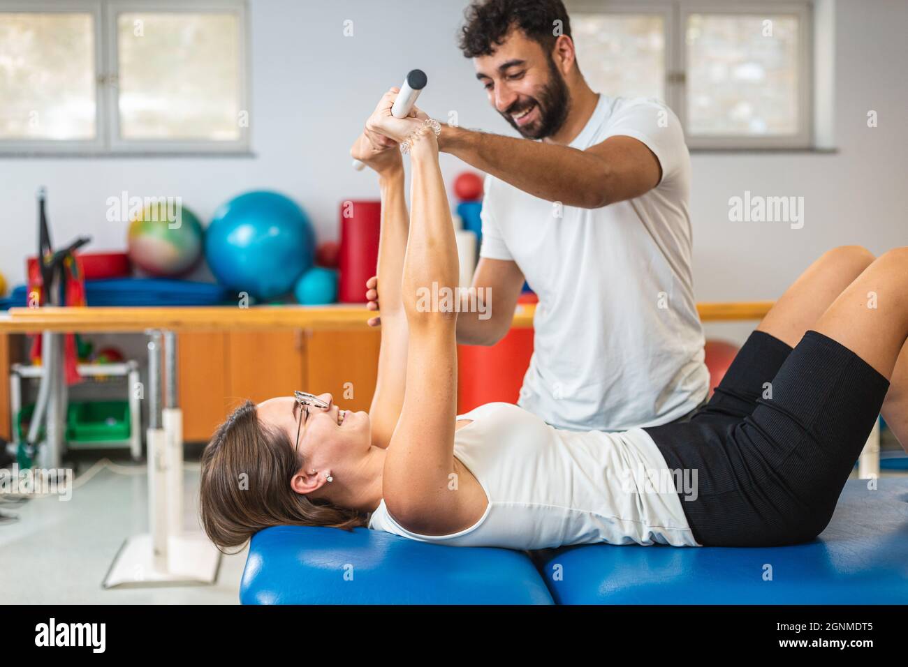 Femme faisant des exercices avec le bar médical, en position de décubitus dorsal. Un physiothérapeute masculin se tenant près d'elle et aide à effectuer les exercices Banque D'Images