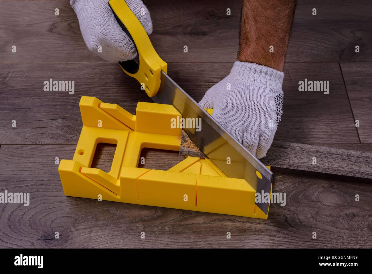 Un homme coupe la plinthe à l'aide d'une scie et d'une boîte à onglets sur  un sol stratifié Photo Stock - Alamy