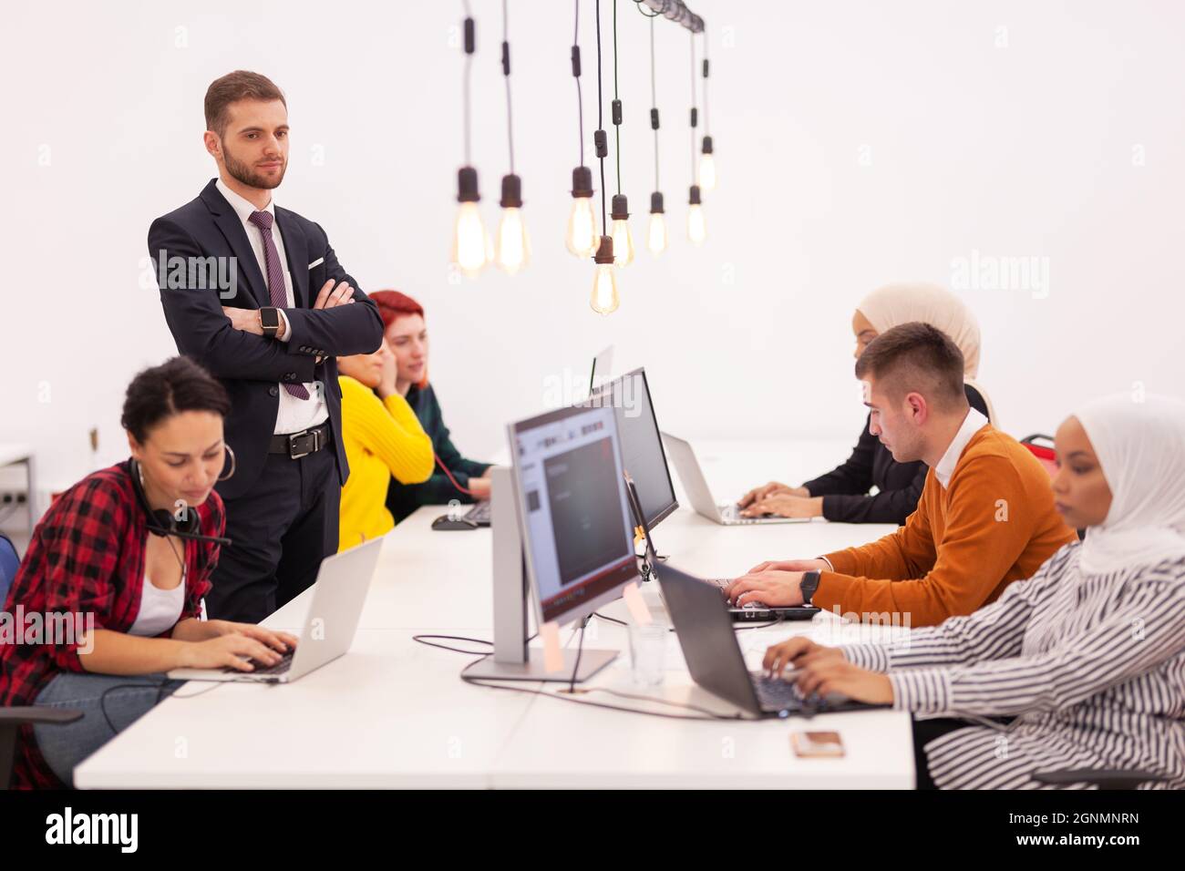 Groupe de collègues multiethniques travaillant sur des ordinateurs de bureau dans un espace de bureau moderne. Fille reposant avec les pieds sur la table Banque D'Images