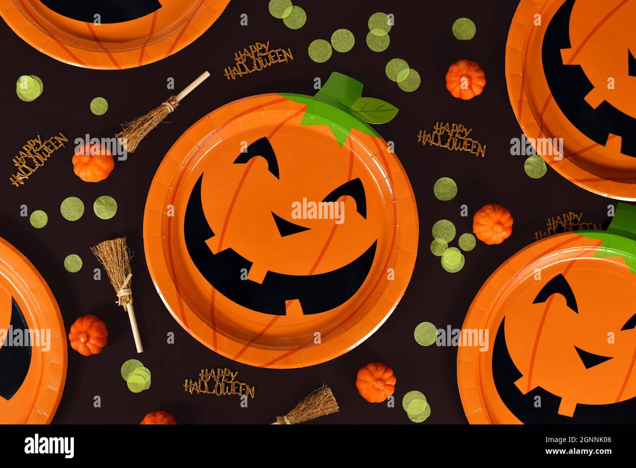 Halloween Party Flat Lay avec des assiettes en papier de citrouille orange, des balais de sorcière, des confetti et Happy Halloween texte sur fond noir Banque D'Images