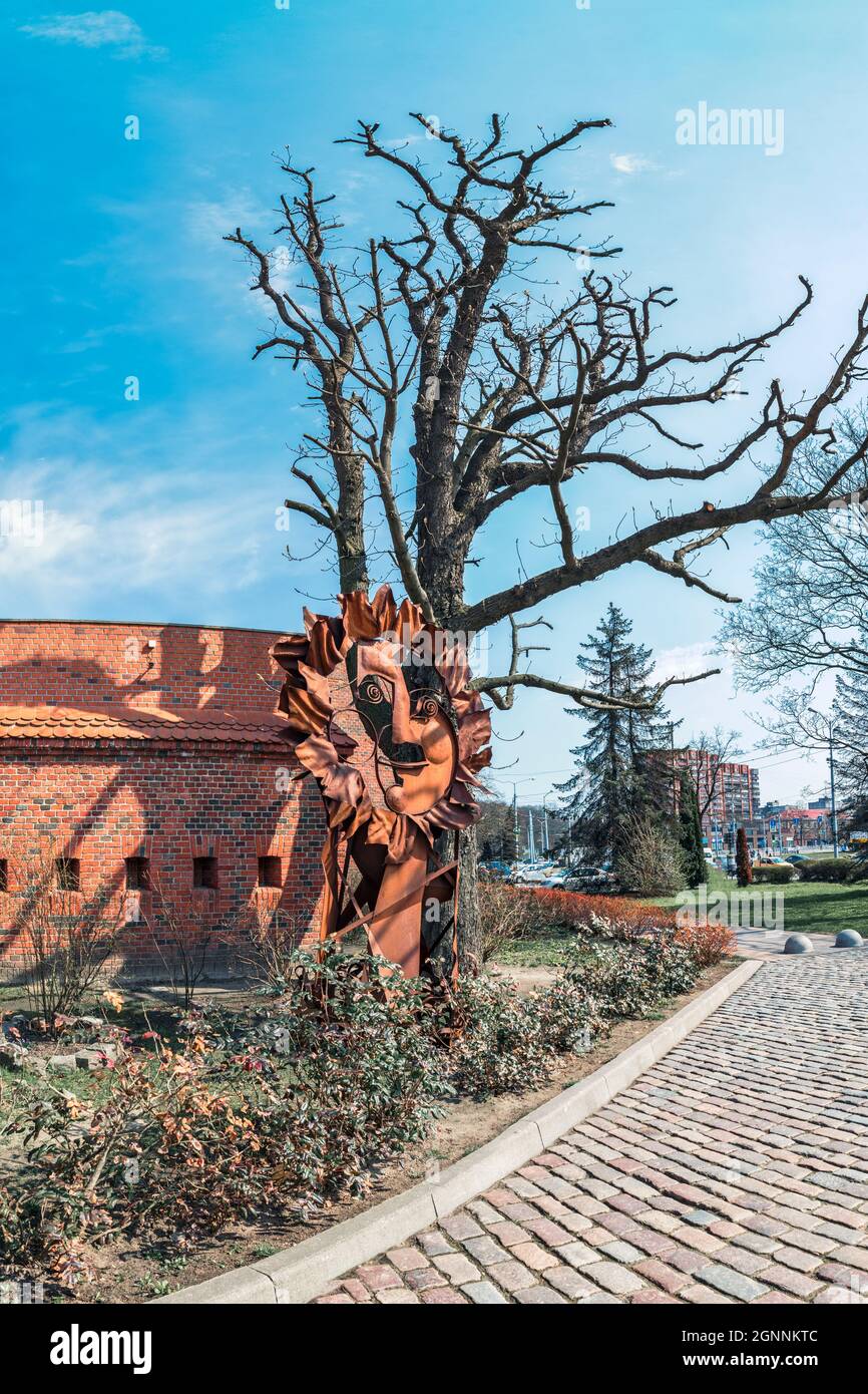 Étrange figure rouillée sous un arbre sans feuilles contre un mur de brique Banque D'Images