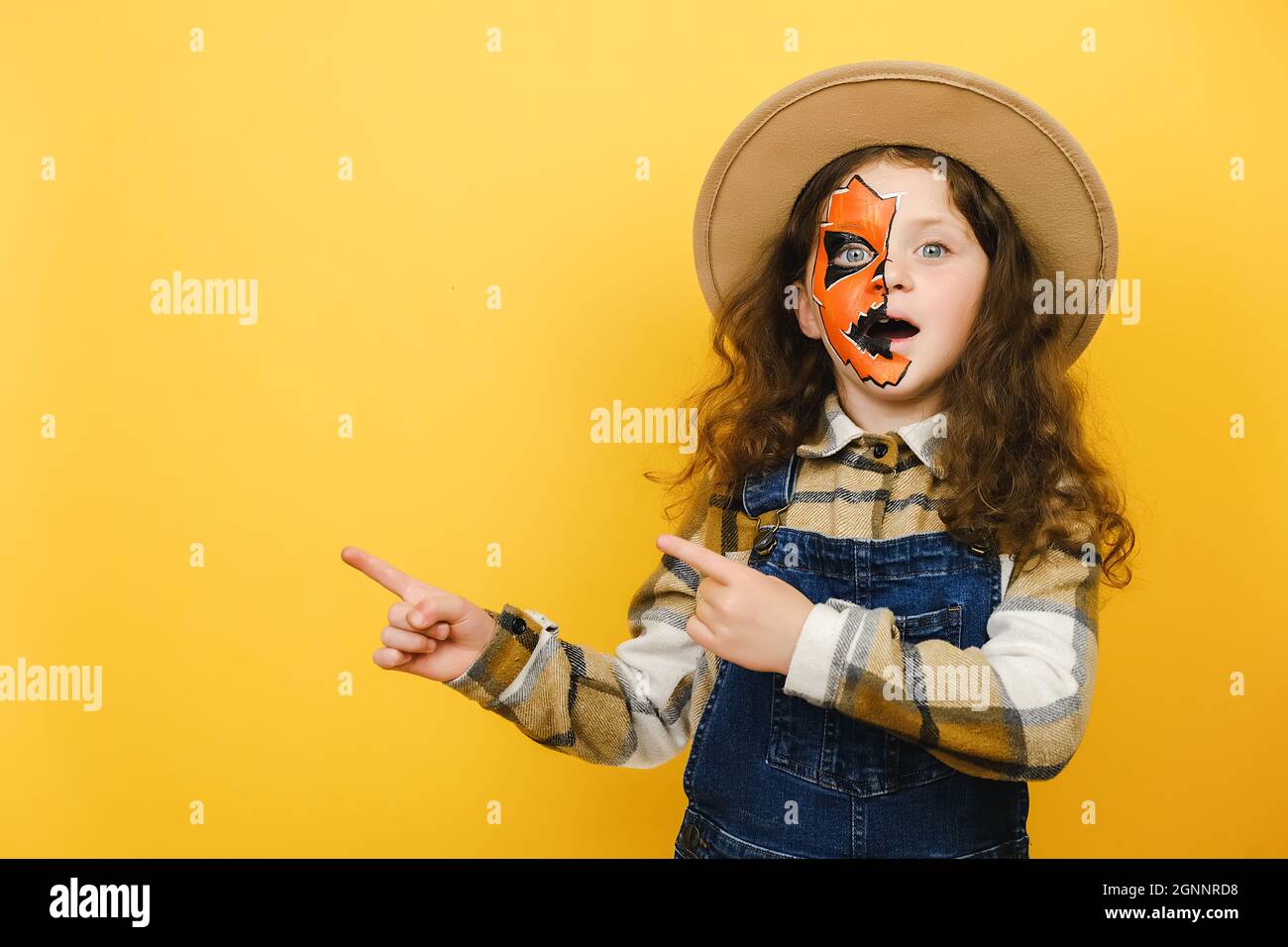 Promoteur choqué petite fille enfant avec Halloween masque de maquillage porte chapeau et chemise, pointe les doigts un côté sur l'espace de travail copier zone de promotion de maquette Banque D'Images