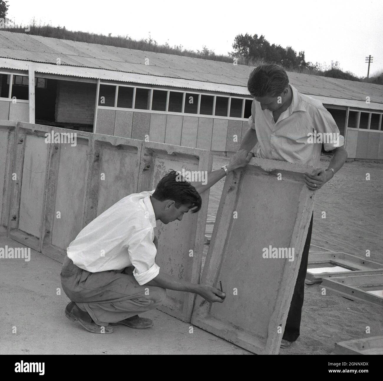 Années 1960, historique, la construction d'un garage préfabriqué dans un local industriel à Witney, Oxford, Angleterre, Royaume-Uni. Deux ouvriers fixent ou boulonnant les panneaux de béton préfabriqué de la laisse inférieure en position. Avec la croissance rapide de la propriété de voiture, il était nécessaire de loger des voitures à partir de la météo et les garages intérieurs construits à partir de panneaux préfabriqués en béton sont devenus un site commun en Grande-Bretagne dans cette époque. Banque D'Images