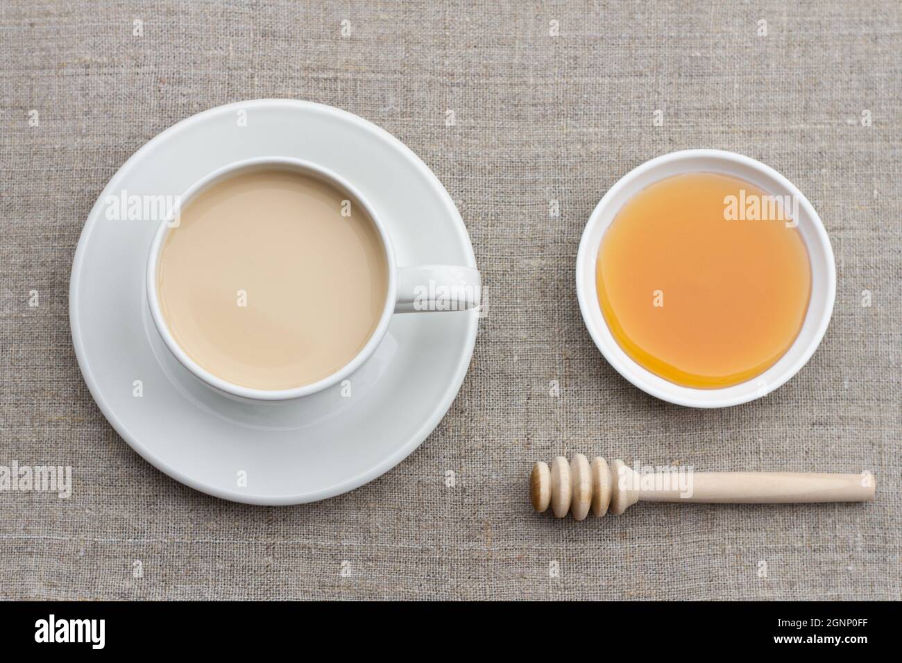 Thé chaud épicé avec du lait dans une tasse en porcelaine blanche avec miel et un panier de miel sur un fond textile Banque D'Images