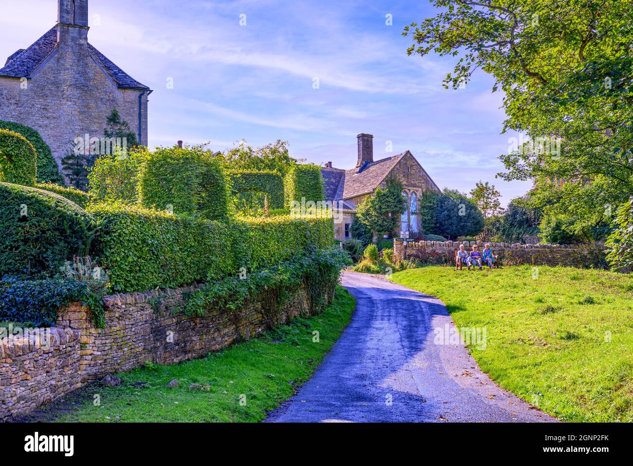 Trois femmes âgées sont assises sur le banc et profitent du soleil matinal dans le joli village des Cotswolds de Upper Slaughter Gloucestershire, Royaume-Uni Banque D'Images