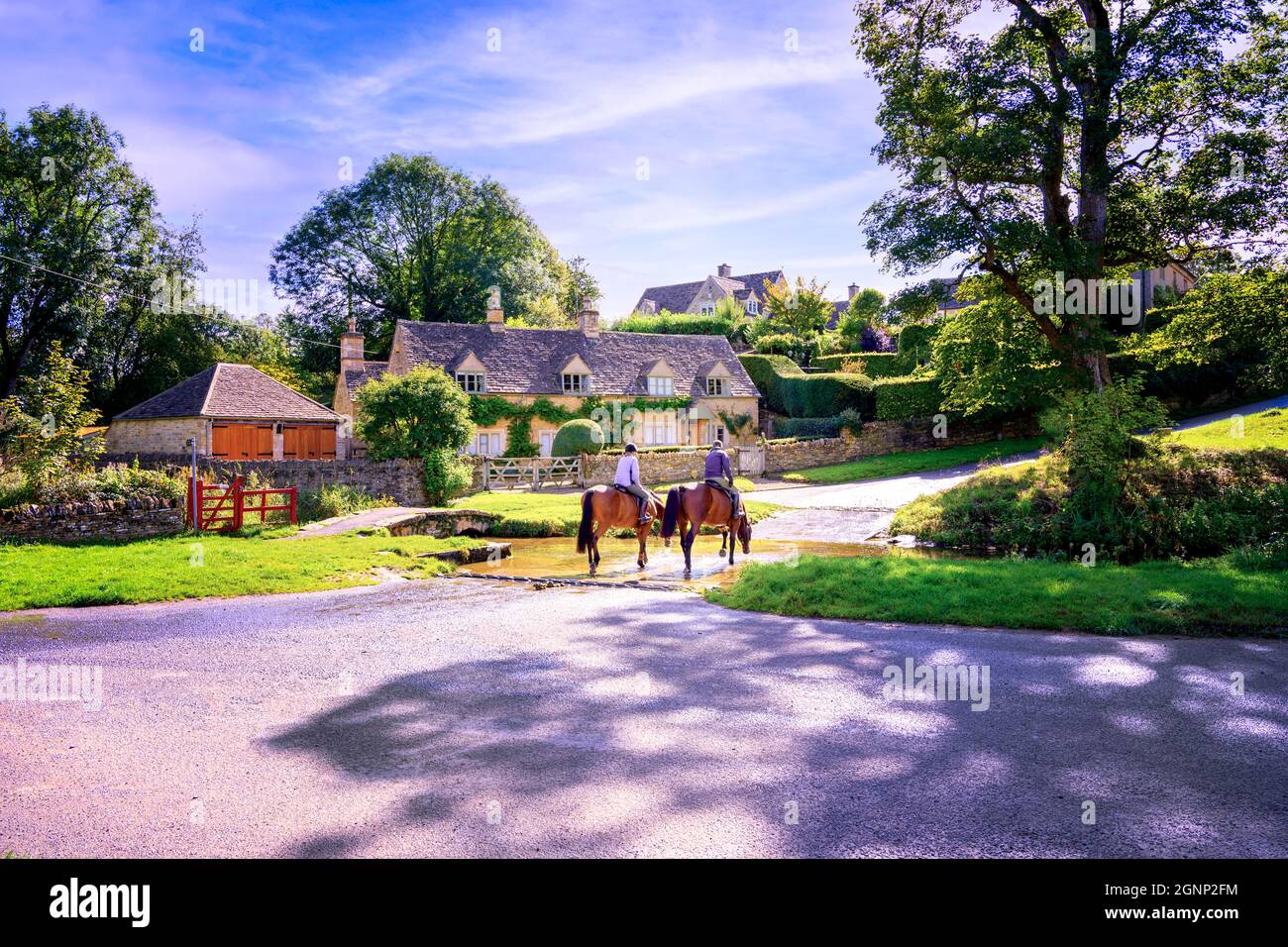 Deux chevaux et cavaliers traversant ford en face de la rivière traditionnelle en pierre construit Cotswold village cottage en arrière-plan. Upper Slaughter Gloucestershire Royaume-Uni Banque D'Images