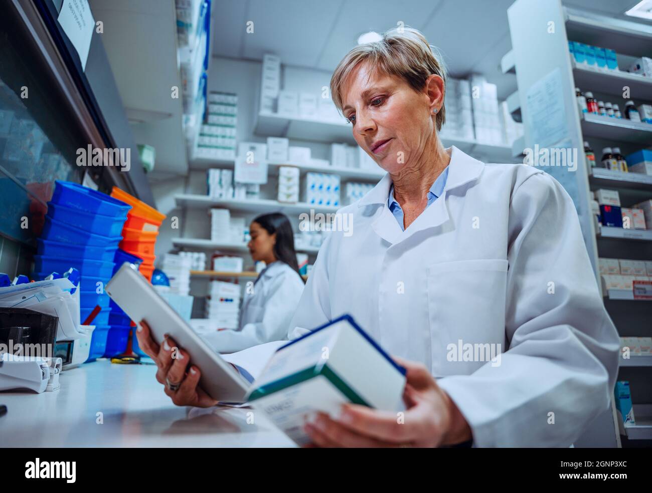 La pharmacienne caucasienne lit les étiquettes sur la boîte de médicaments d'ordonnance qui se trouve dans la pharmacie Banque D'Images