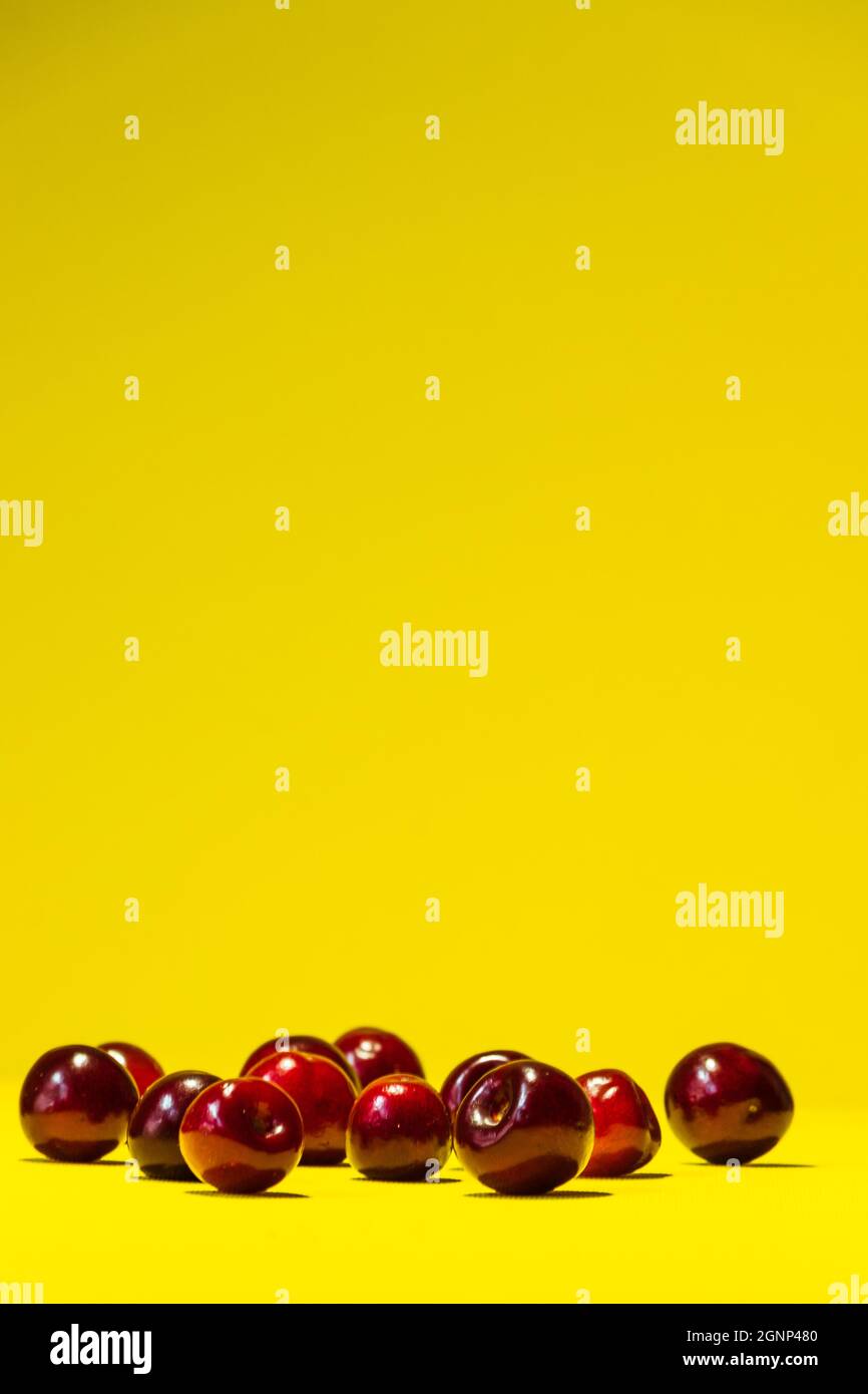 Un bouquet de cerises rouges repose chaotiquement sur un fond jaune vif d'été. Banque D'Images
