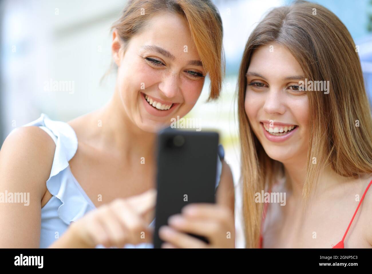 Deux amis heureux utilisant un smartphone et riant dans la rue Banque D'Images
