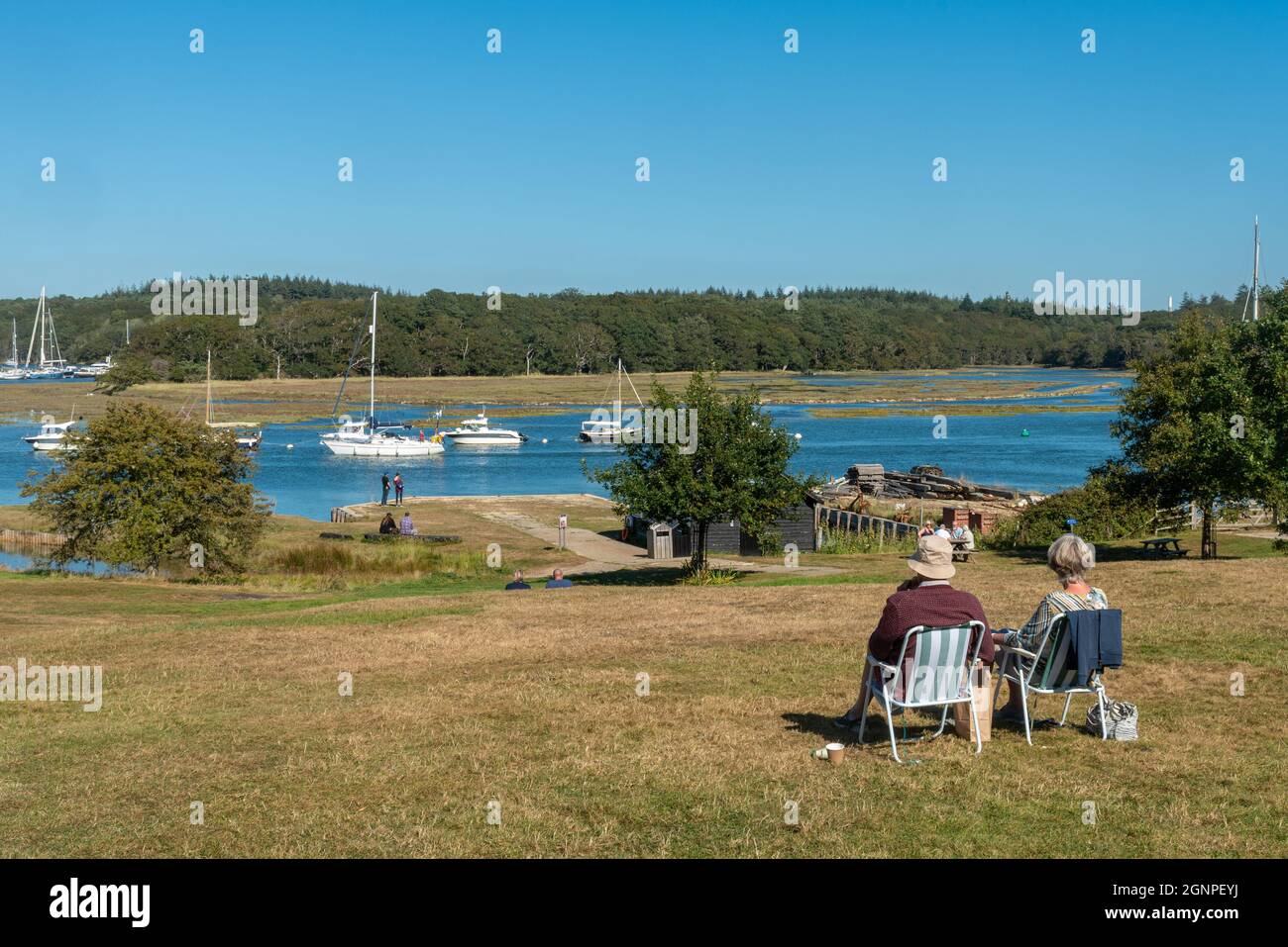 Les gens s'asseyant et profitant d'une journée ensoleillée regardant les bateaux et les yachts sur la rivière Beaulieu depuis le village de Bucklers Hard dans la New Forest, Hampshire, Royaume-Uni Banque D'Images