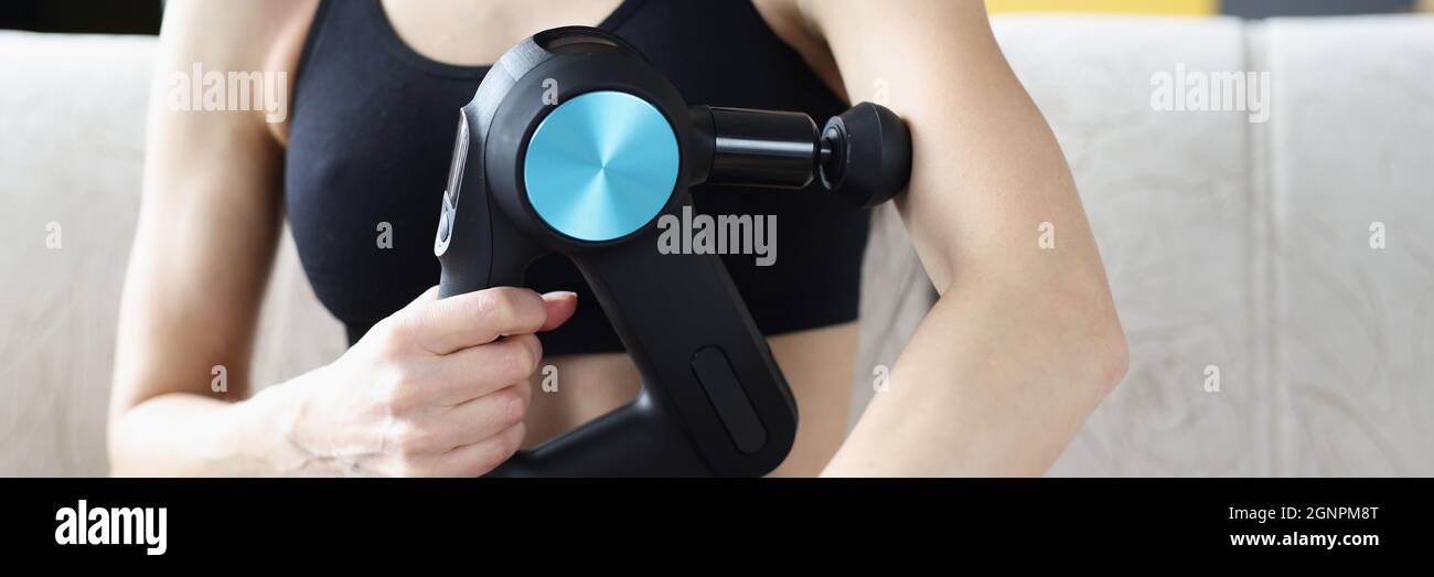 Jeune femme effectuant un massage avec un masseur à percussion à la maison Banque D'Images
