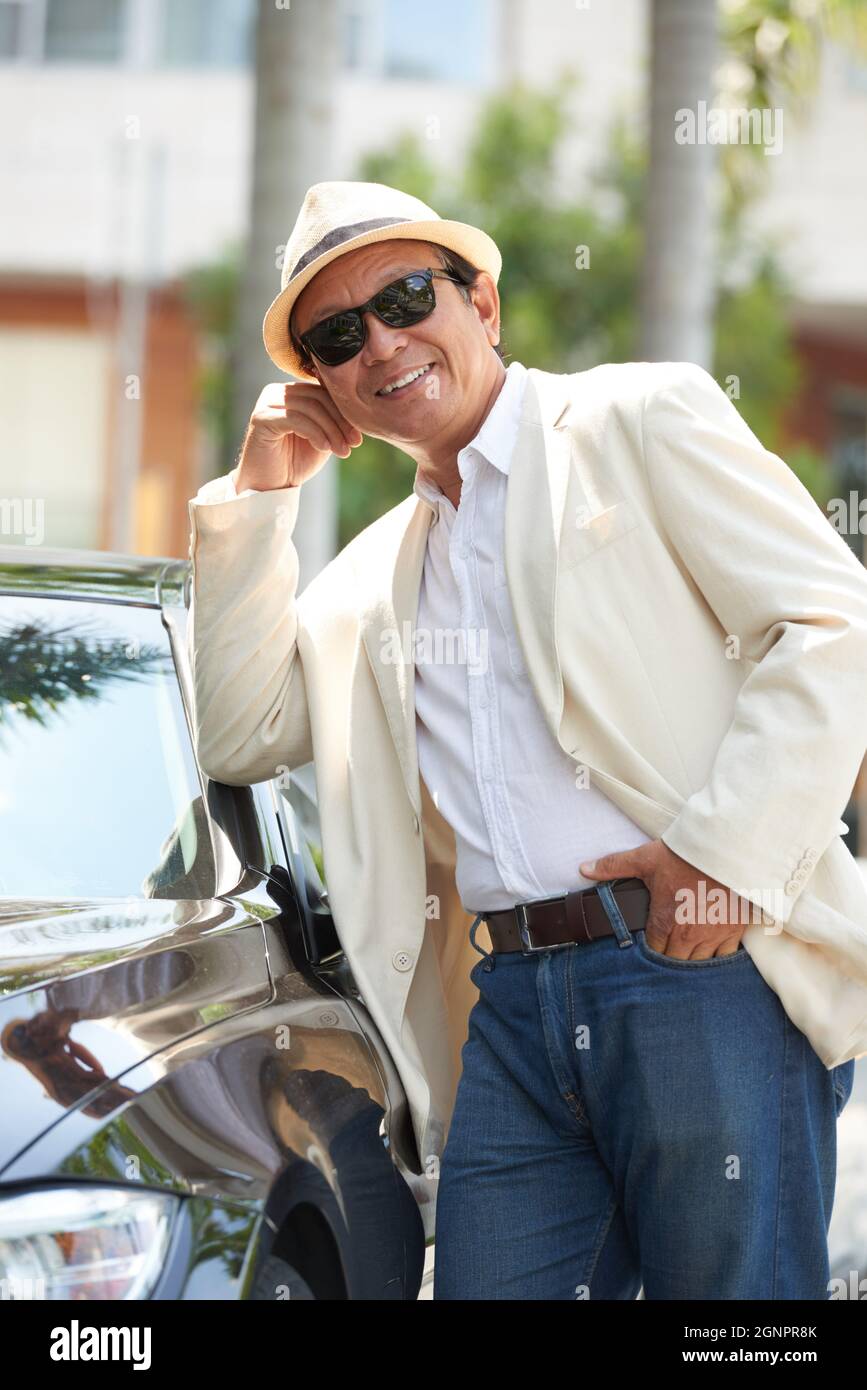 Portrait d'un homme vietnamien riche et heureux en veste blanche et lunettes de soleil se penchant sur la voiture à l'extérieur Banque D'Images
