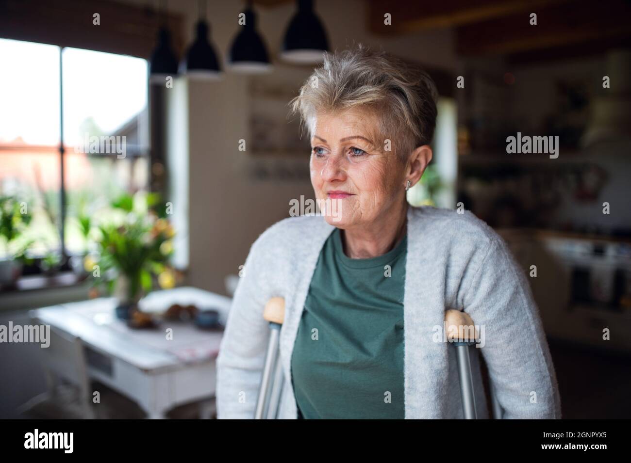 Portrait d'une femme âgée avec des béquilles à l'intérieur à la maison, en regardant de côté. Banque D'Images