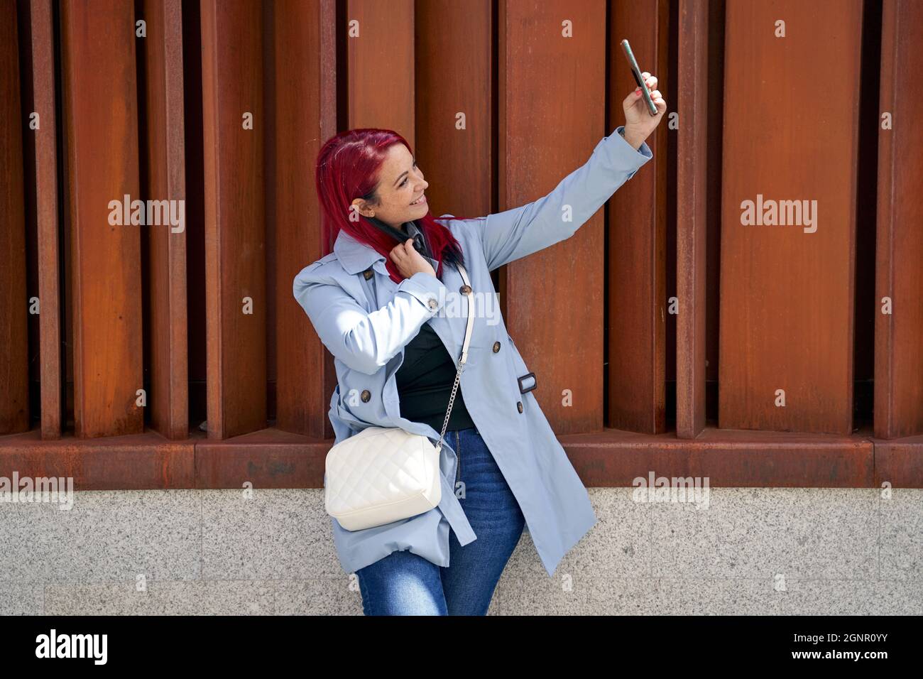 Belle femme à tête rouge prenant un selfie avec son smartphone dans une rue de la ville. Photo de haute qualité Banque D'Images