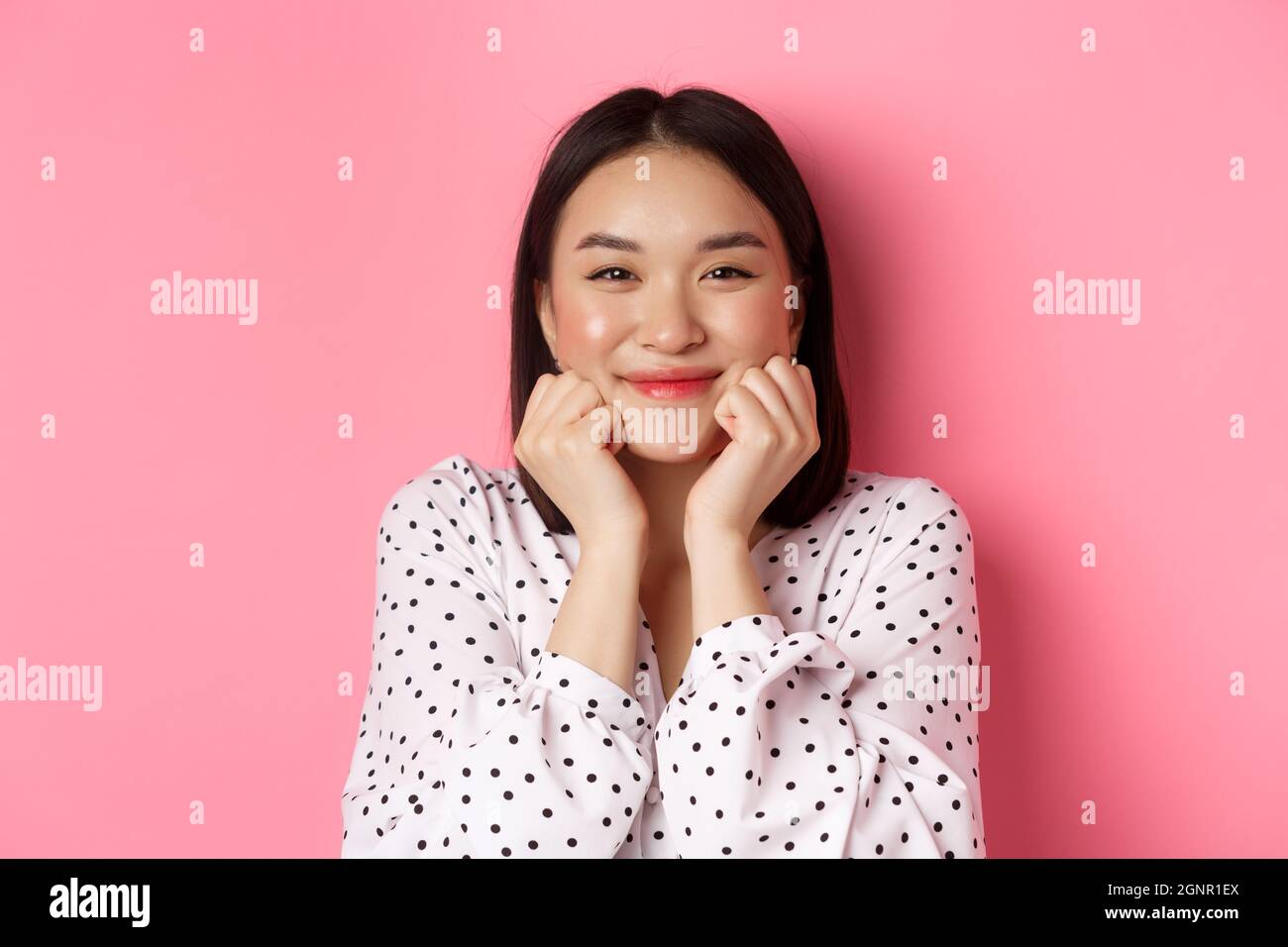 Concept de beauté et de style de vie. Gros plan d'une adorable femme asiatique montrant des joues bouffies, souriant et ravie, debout sur fond rose. Banque D'Images