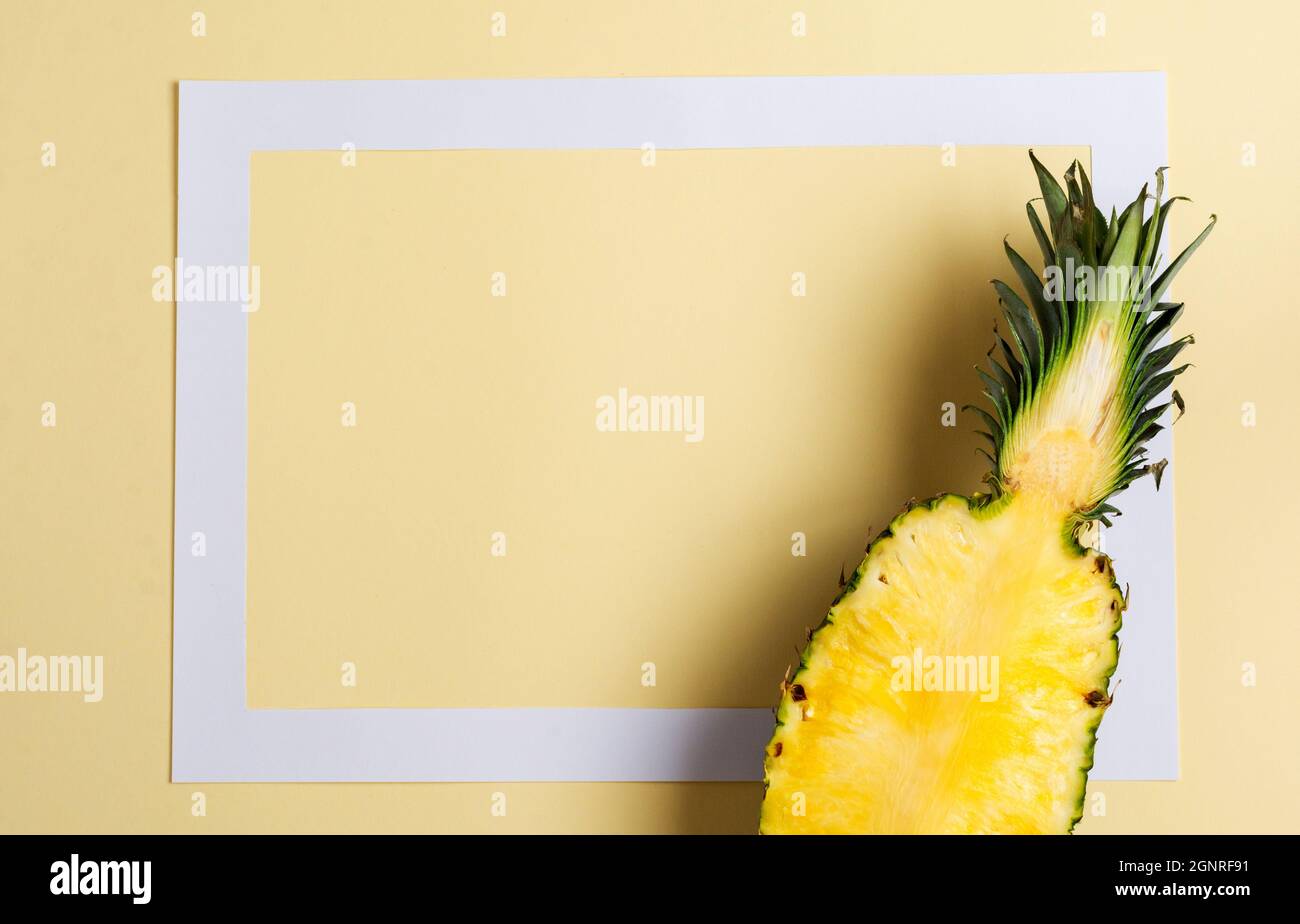 Ananas frais coupé en deux parties et cadre en papier sur fond jaune. Concept d'été. Plan de travail créatif avec espace de copie. Vue de dessus Banque D'Images