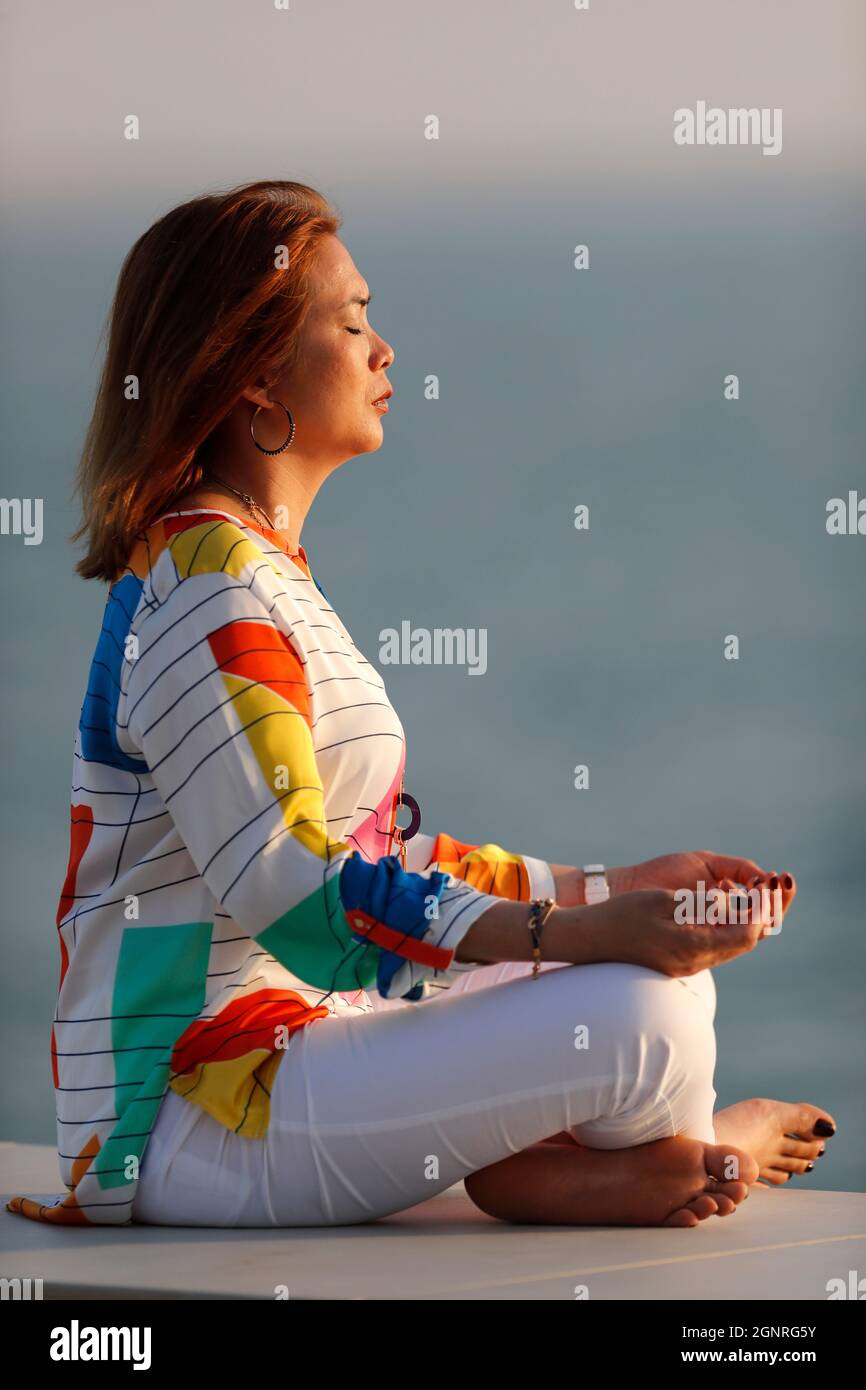 Femme ayant la méditation de yoga sur la mer avant le coucher du soleil. Silence et relaxation concept. Banque D'Images