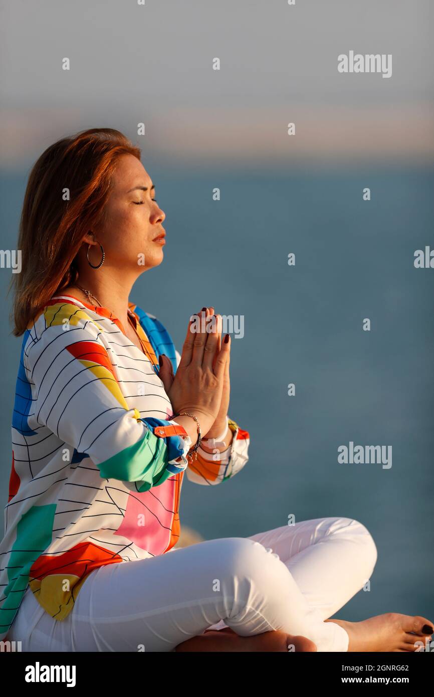 Femme ayant la méditation de yoga sur la mer avant le coucher du soleil. Silence et relaxation concept. Banque D'Images