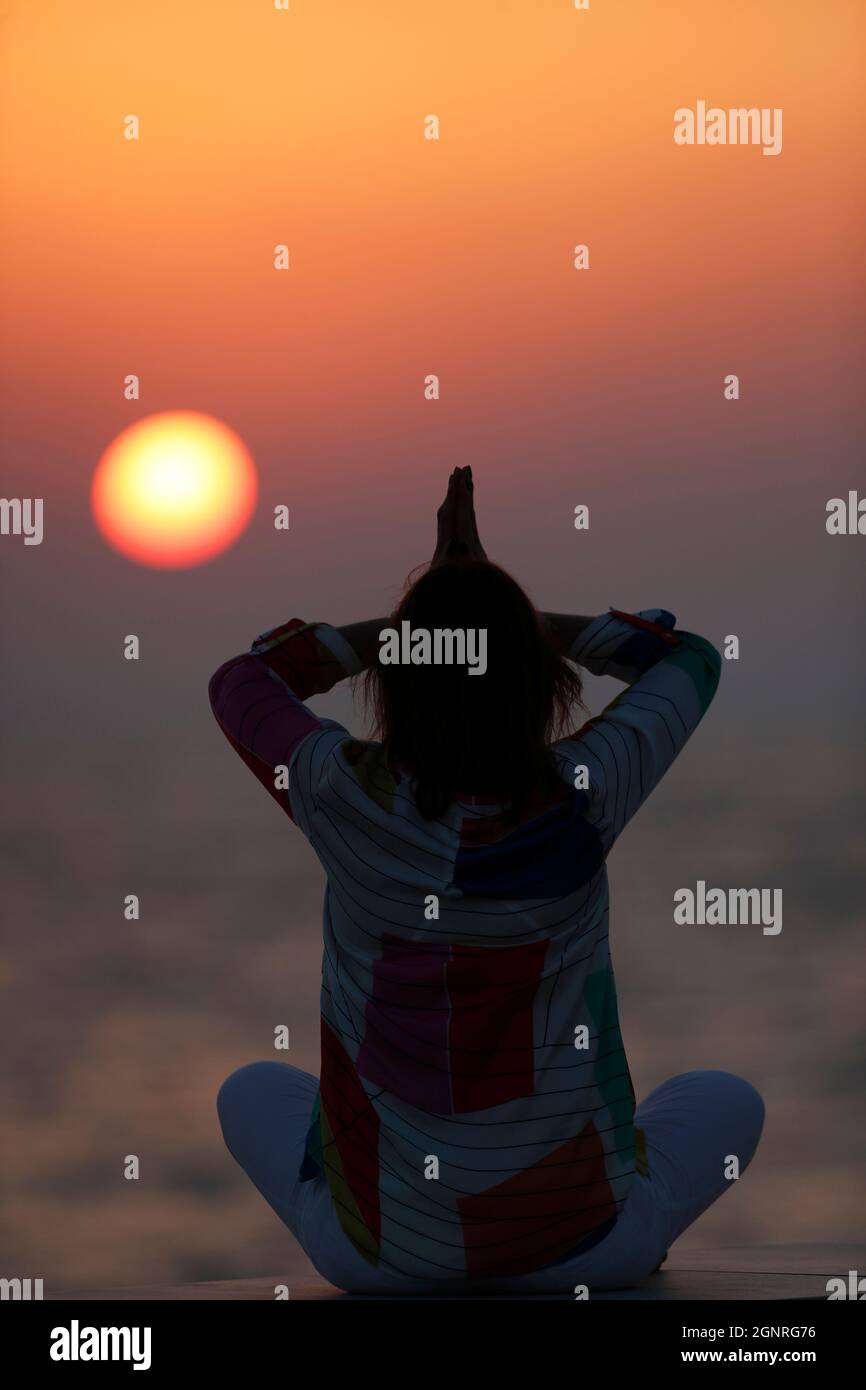 Femme ayant la méditation de yoga sur la plage au coucher du soleil. Silence et relaxation concept. Banque D'Images