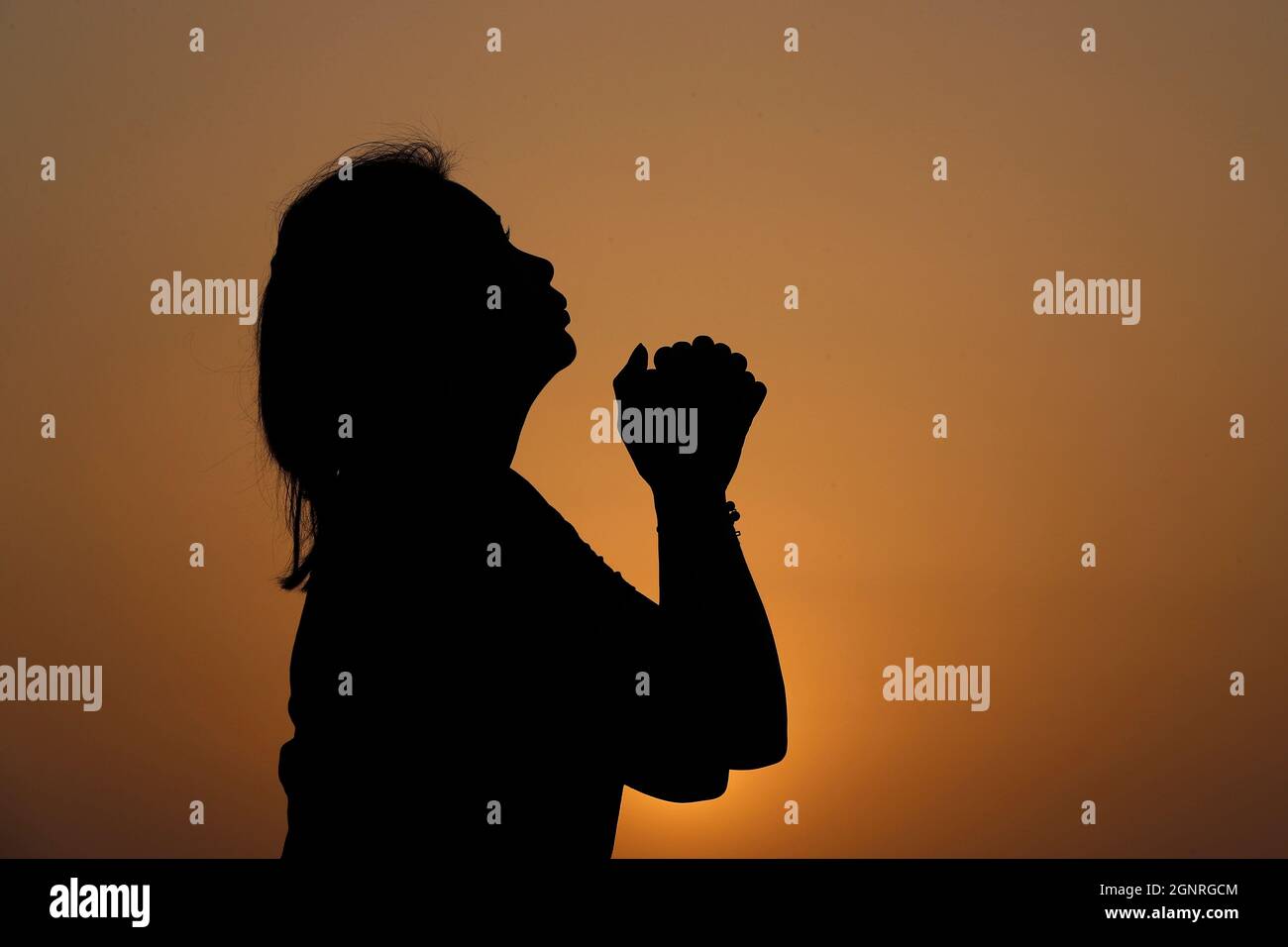 Silhouette au coucher du soleil de la femme fidèle priant, les mains se replient dans l'adoration à dieu. Concept de religion, de foi, de prière et de spiritualité. Banque D'Images