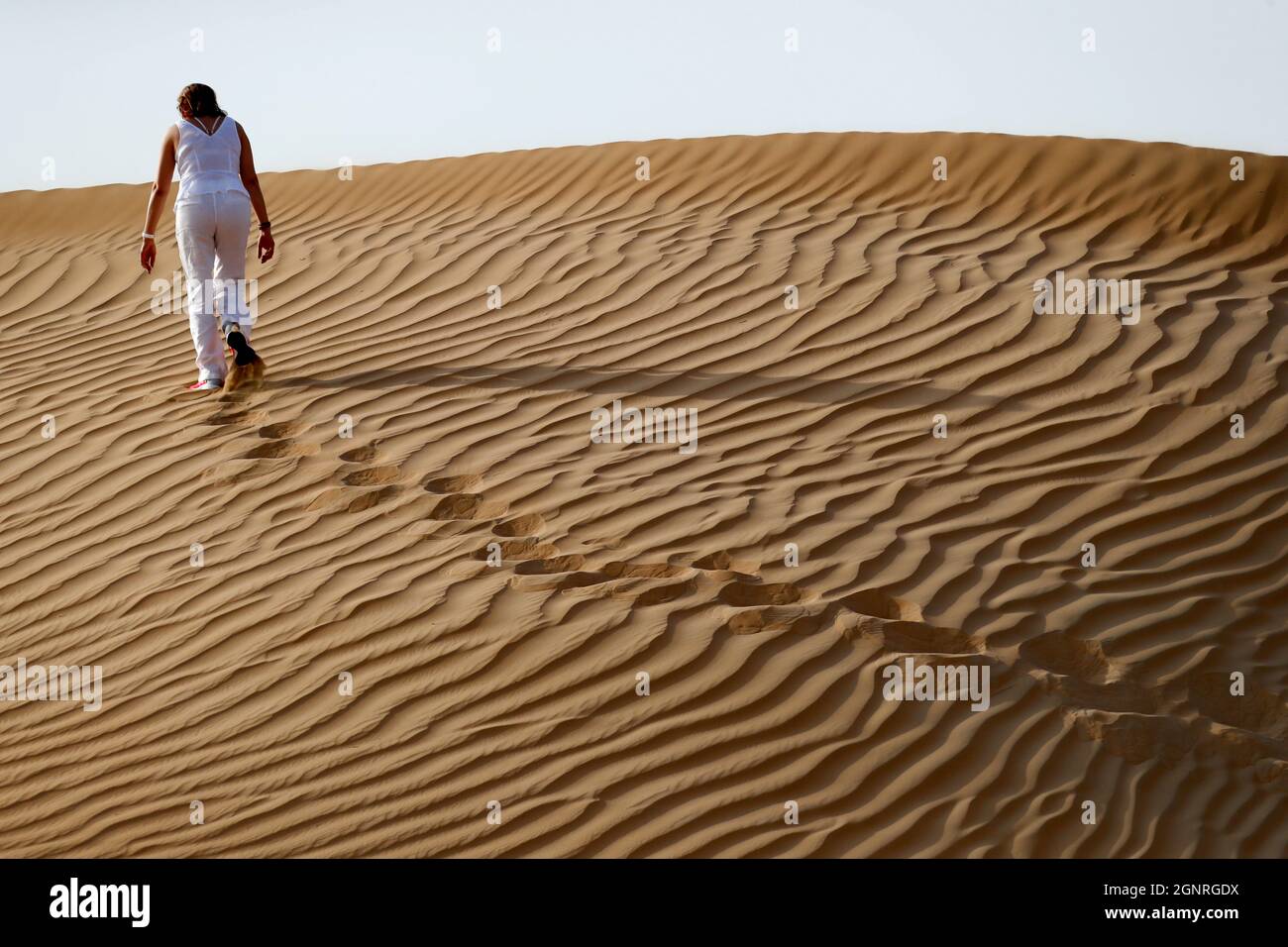 Femme laissant des empreintes de pas et allant jusqu'à la dune de sable du désert. Dubaï. Émirats arabes Unis. Banque D'Images