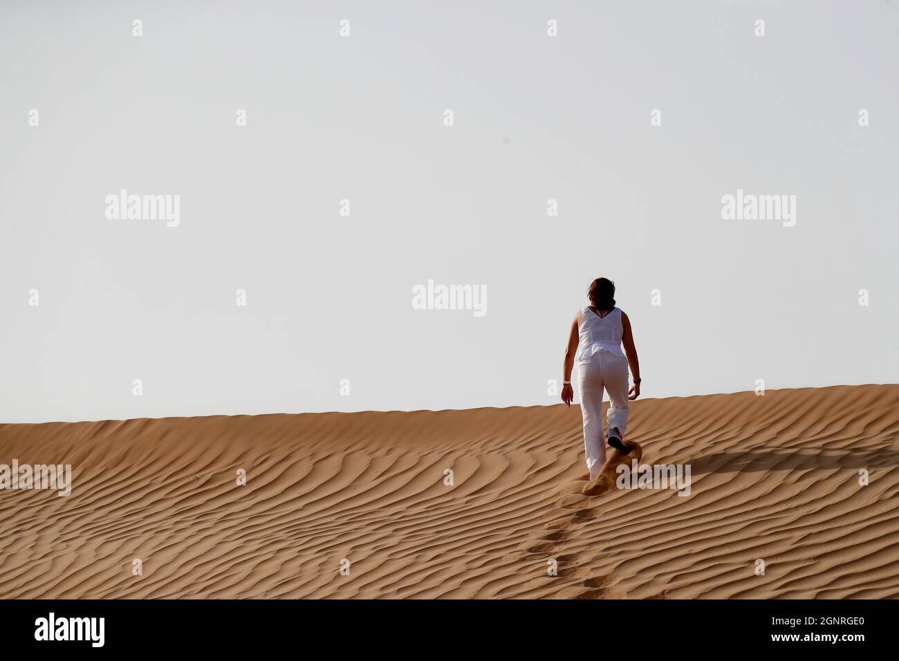 Femme laissant des empreintes de pas et allant jusqu'à la dune de sable du désert. Dubaï. Émirats arabes Unis. Banque D'Images