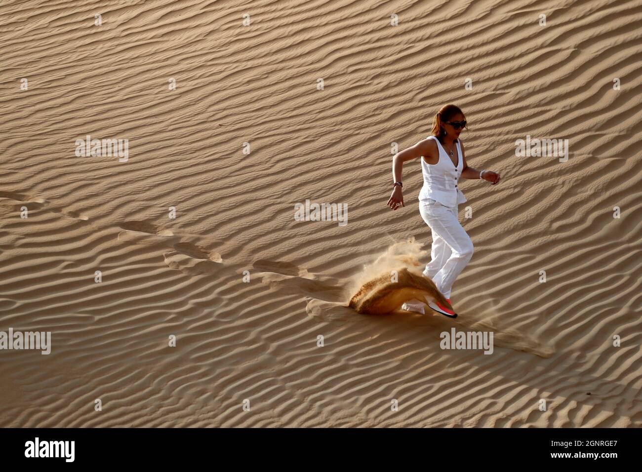 Femme laissant des empreintes de pas et descendant une dune de sable du désert. Dubaï. Émirats arabes Unis. Banque D'Images
