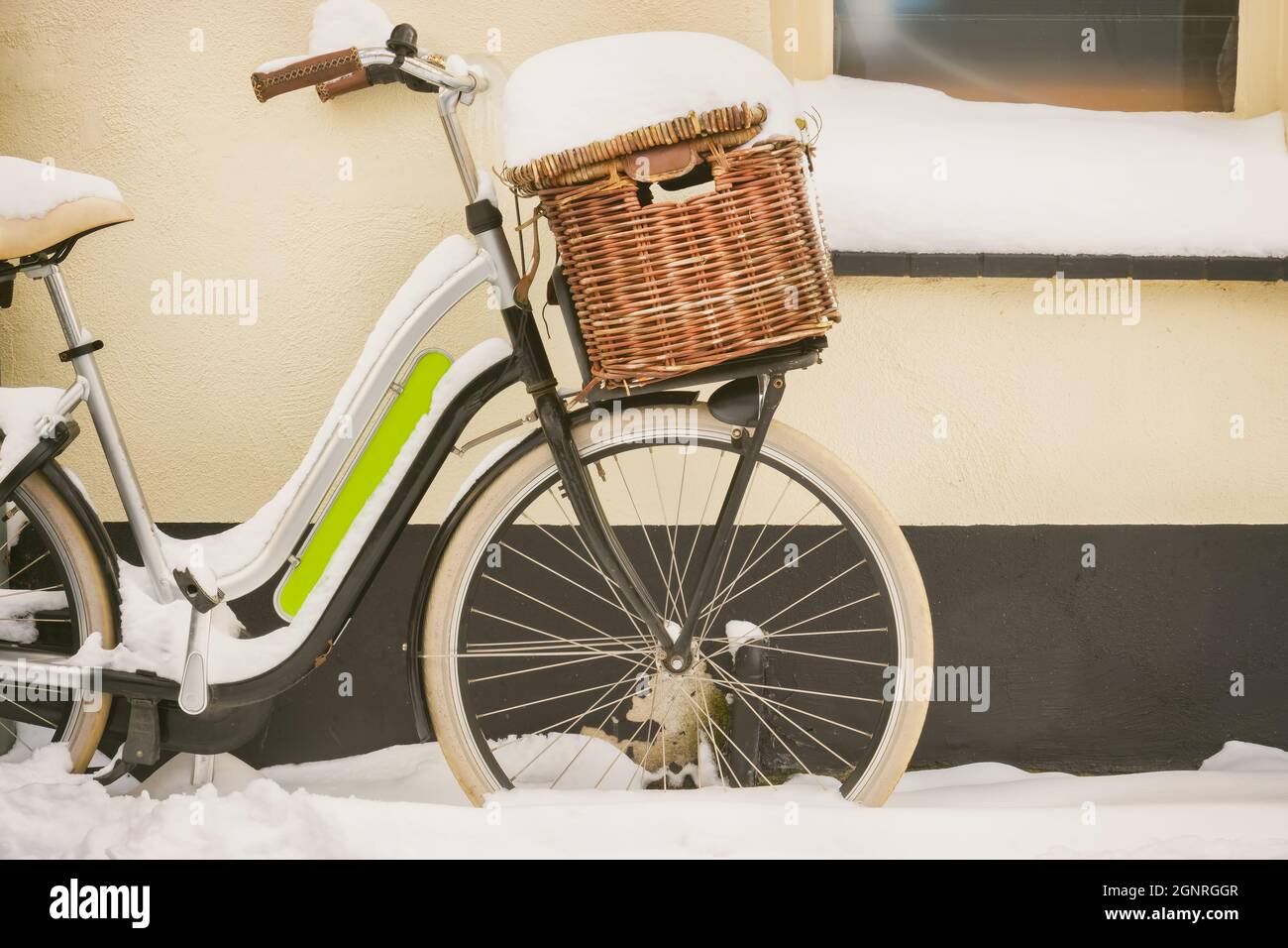 Vélo hollandais avec panier recouvert de neige pendant l'hiver, garé à l'extérieur d'une vieille maison Banque D'Images