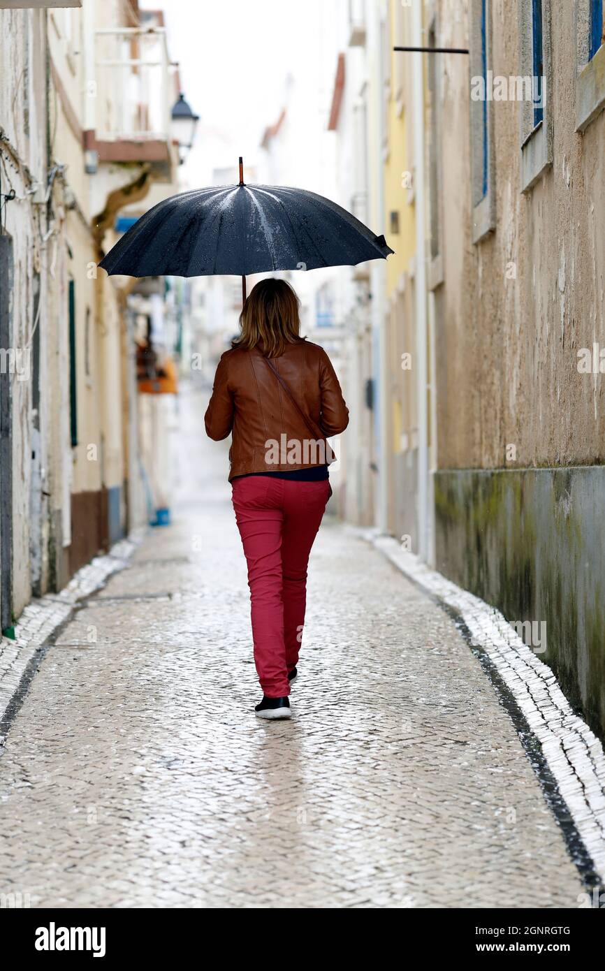 Vue arrière d'une femme avec parasol noir marchant dans la rue. Nazaré. Portugal. Banque D'Images