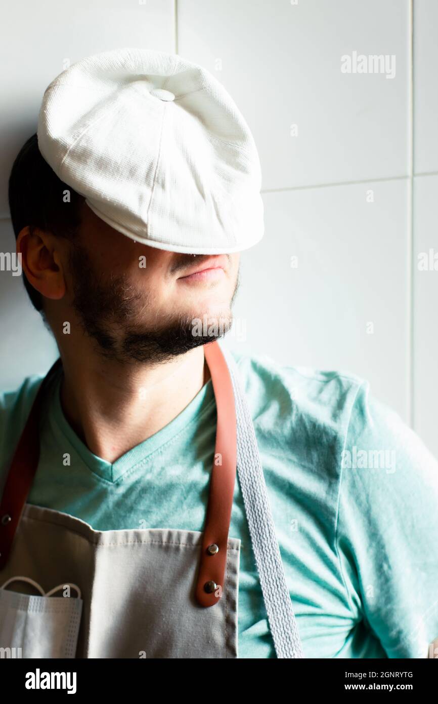 Un jeune boulanger dans une casquette et un tablier dort sur un travail dans une boulangerie. Concept de fatigue. Banque D'Images