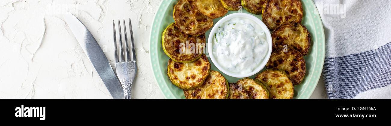 Bannière de tranches de courgettes frites avec sauce à la crème aigre sur l'assiette. Courgettes frites aux herbes pour le dîner sur fond blanc. Haut wiev Banque D'Images