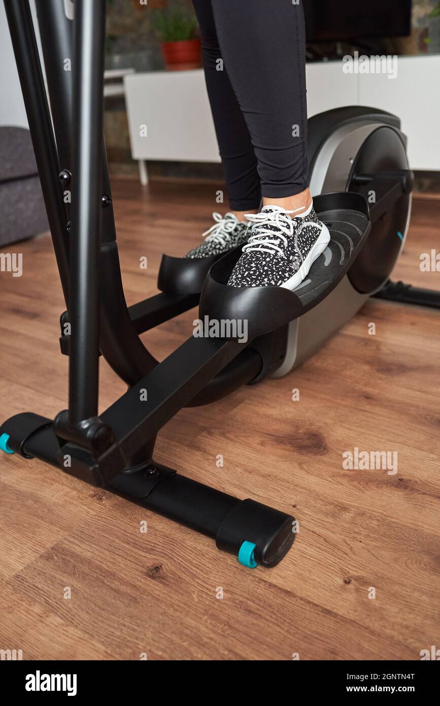 Jambes de femme entraînement sur vélo elliptique dans le salon à la maison Banque D'Images